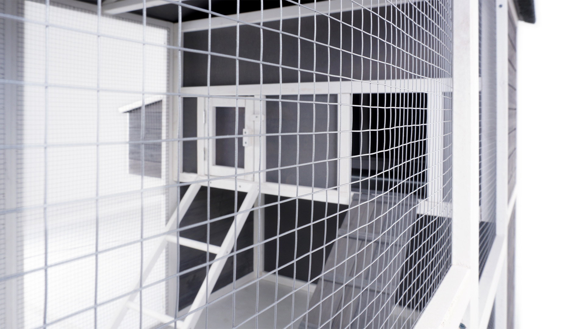 Ein grau-weißes Holztierhaus mit Drahtgitterwänden. Innen sind eine kleine Box und eine Rampe sichtbar.