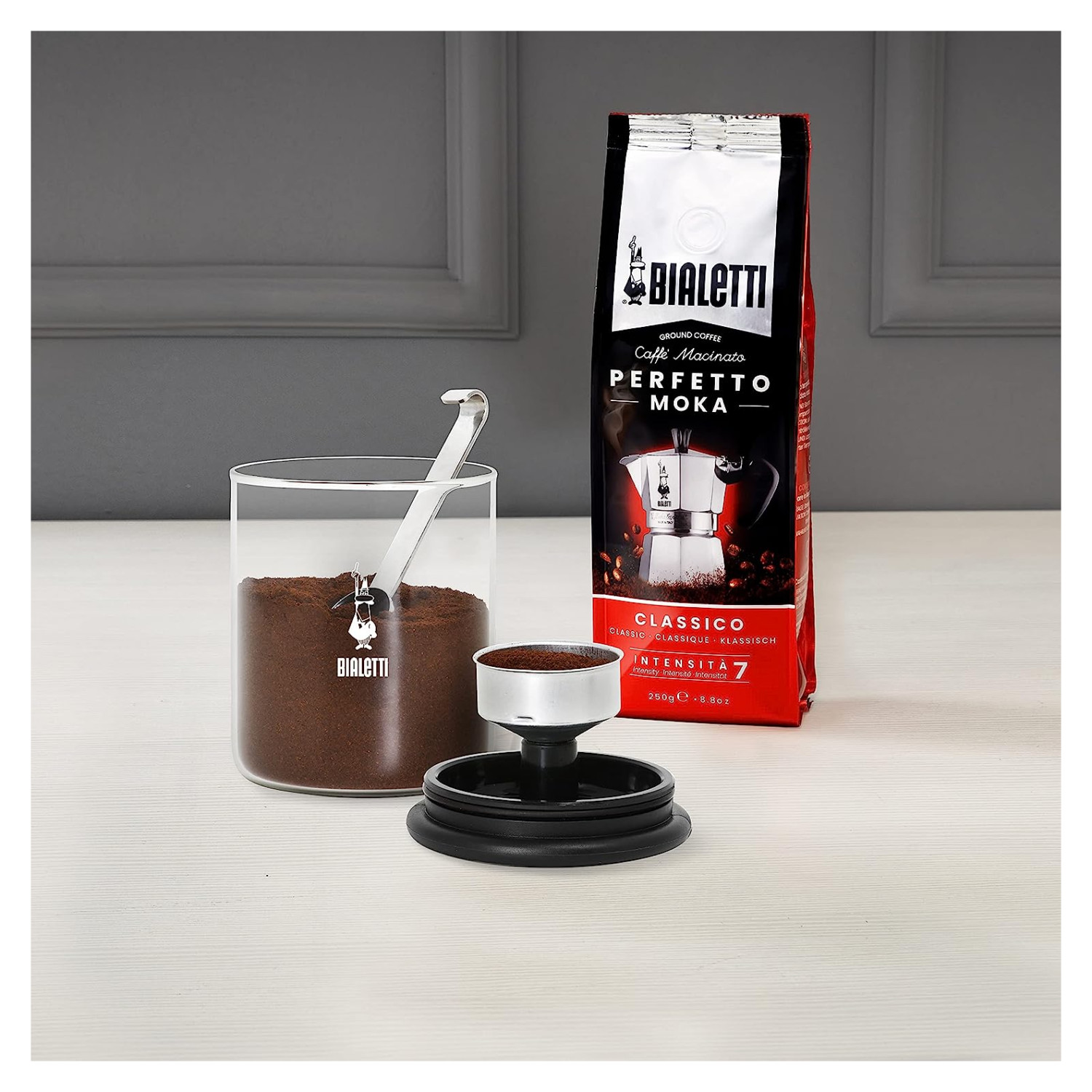 Caffè Bialetti: Vaso di vetro con caffè macinato, paletta, filtro e sacchetto caffè rosso.