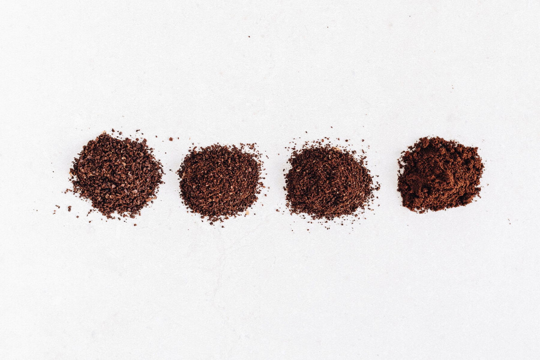 Vier Haufen gemahlenen Kaffees mit unterschiedlichen Körnungen, auf weißem Hintergrund.
