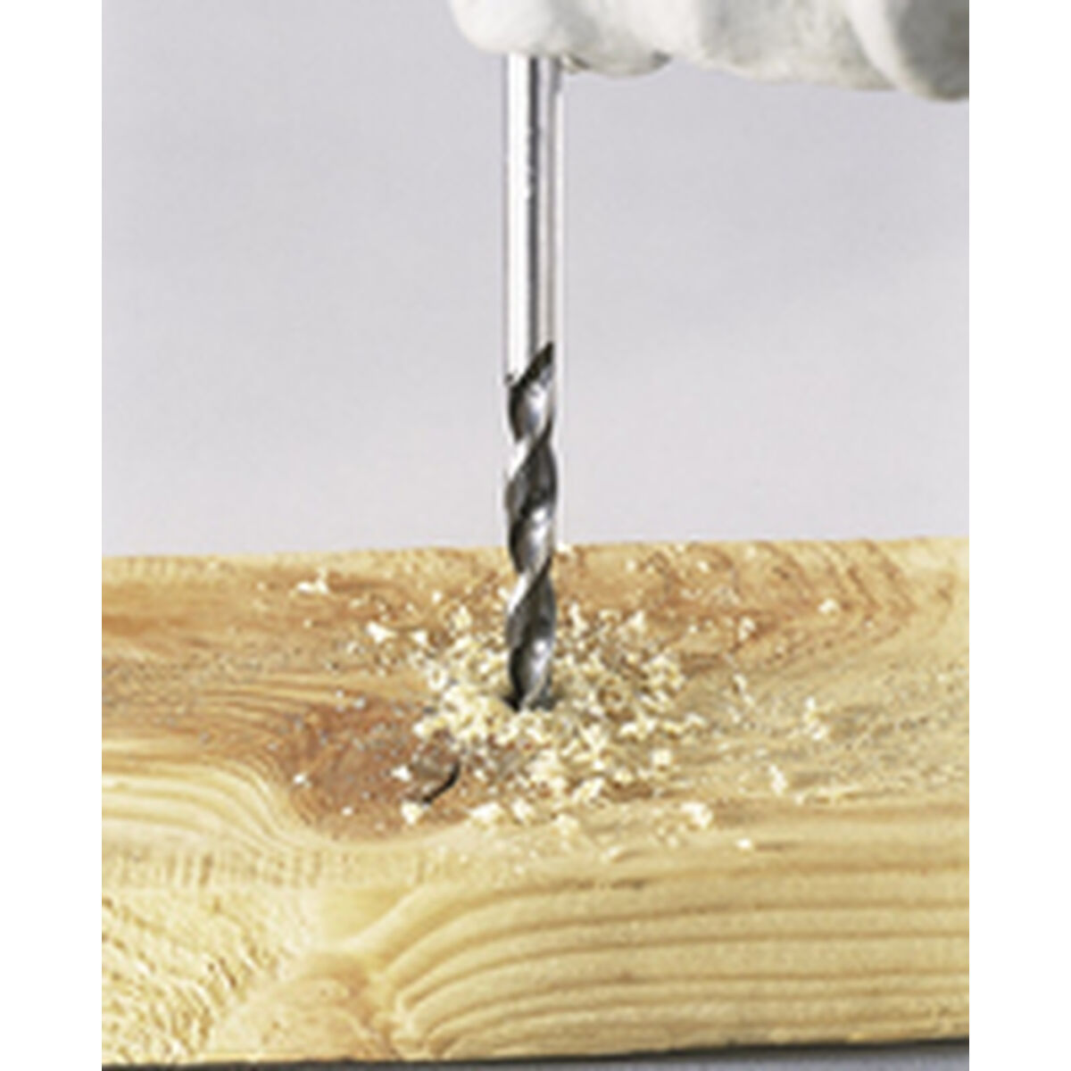 Una broca perforando una tabla de madera, con virutas visibles, primer plano.