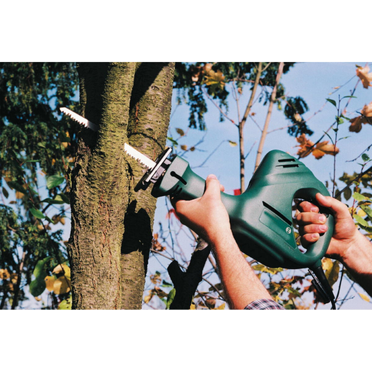 Persona usando una sierra recíproca verde para cortar el tronco de un árbol.
