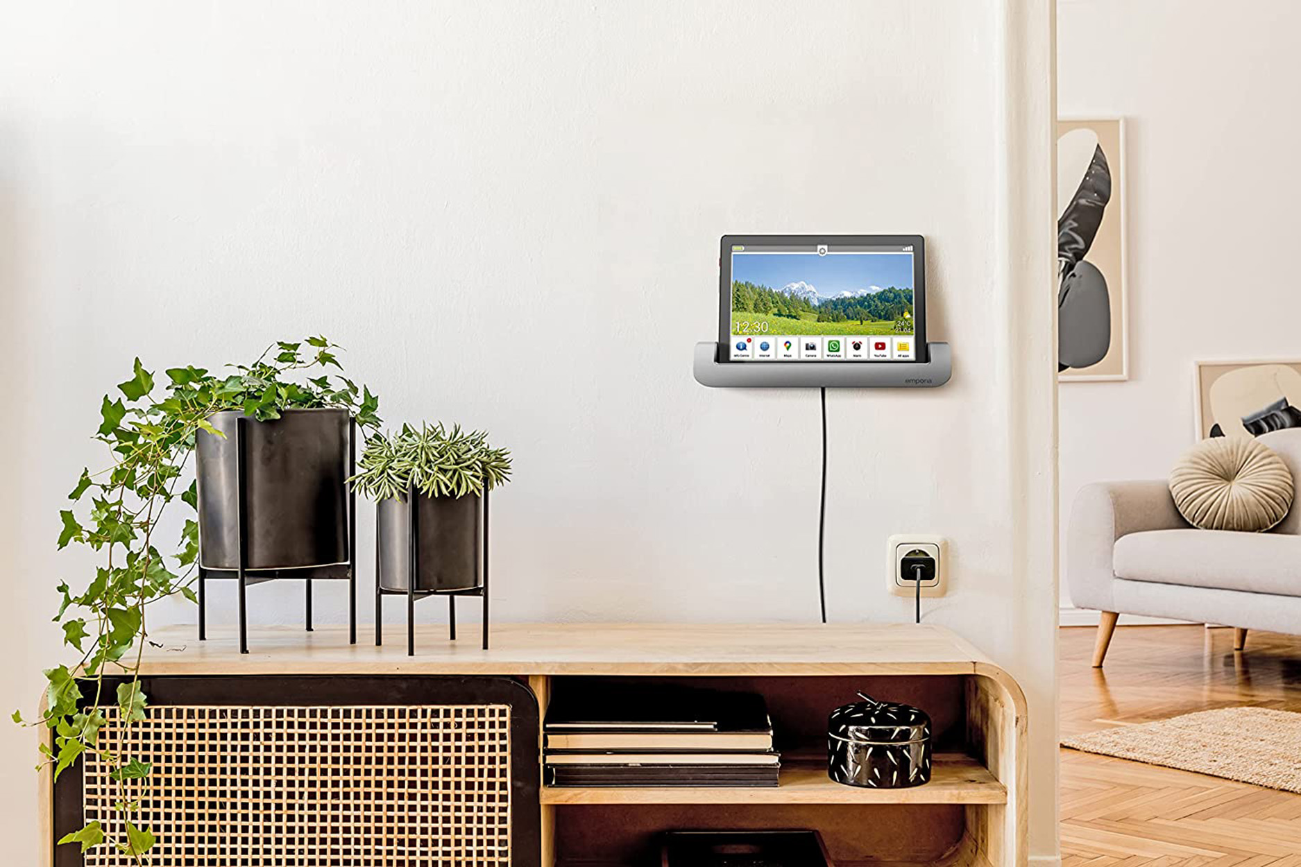 Ein Tablet an der Wand montiert, mit Netzkabel und Pflanzen im Raum.
