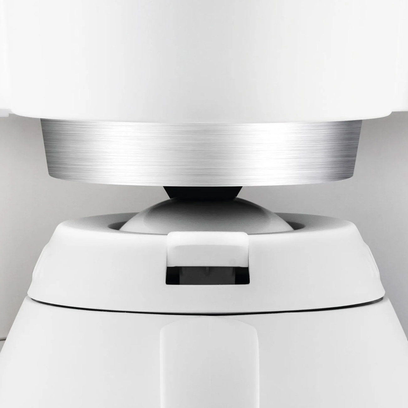 Zbliżenie białego elementu urządzenia ze srebrnym pierścieniem i czarnym środkiem.