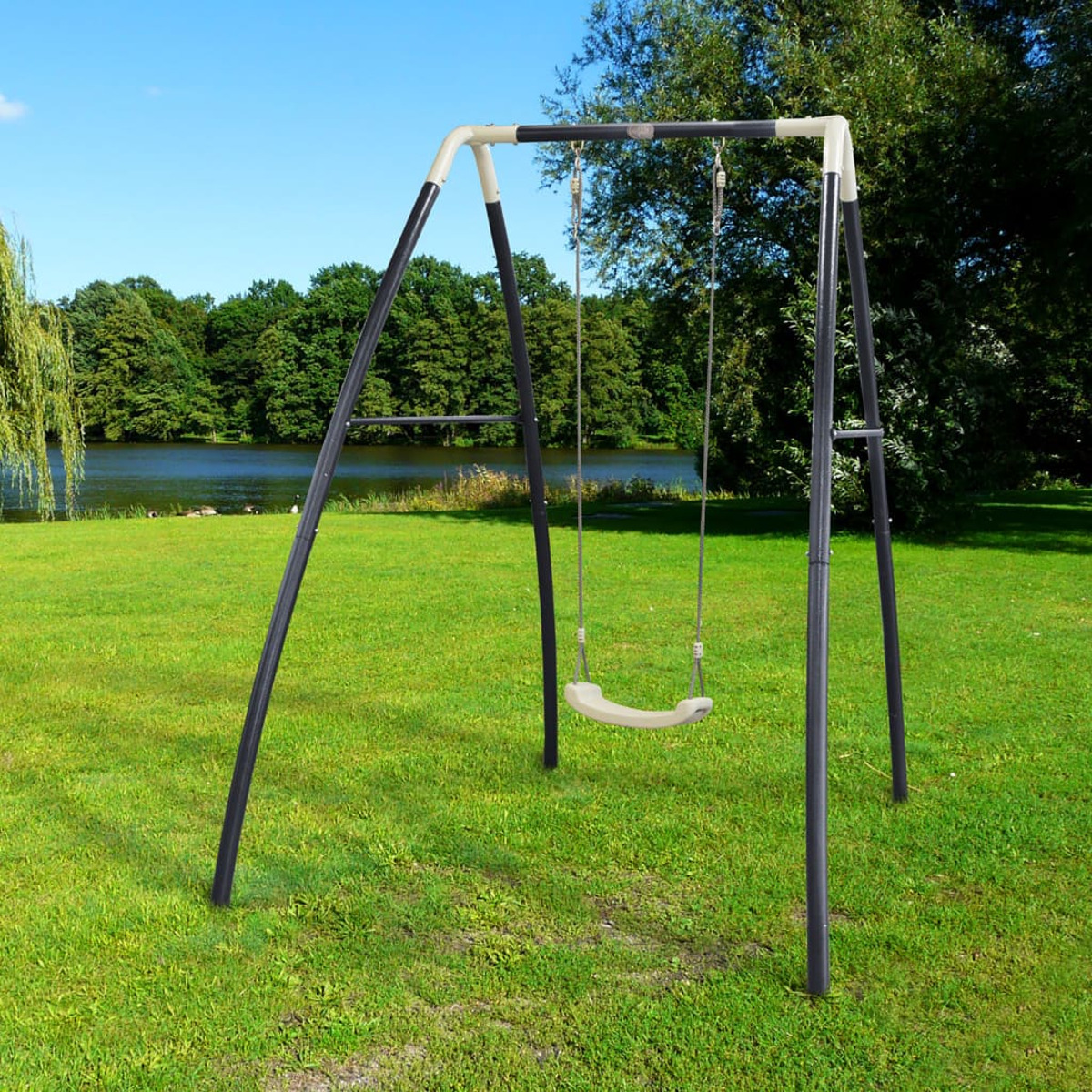 Schaukel auf grünem Gras mit See und Bäumen im Hintergrund. Blauer Himmel.