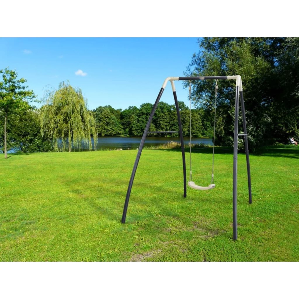 Eine Schaukel auf einer grünen Wiese mit Bäumen und einem See im Hintergrund.