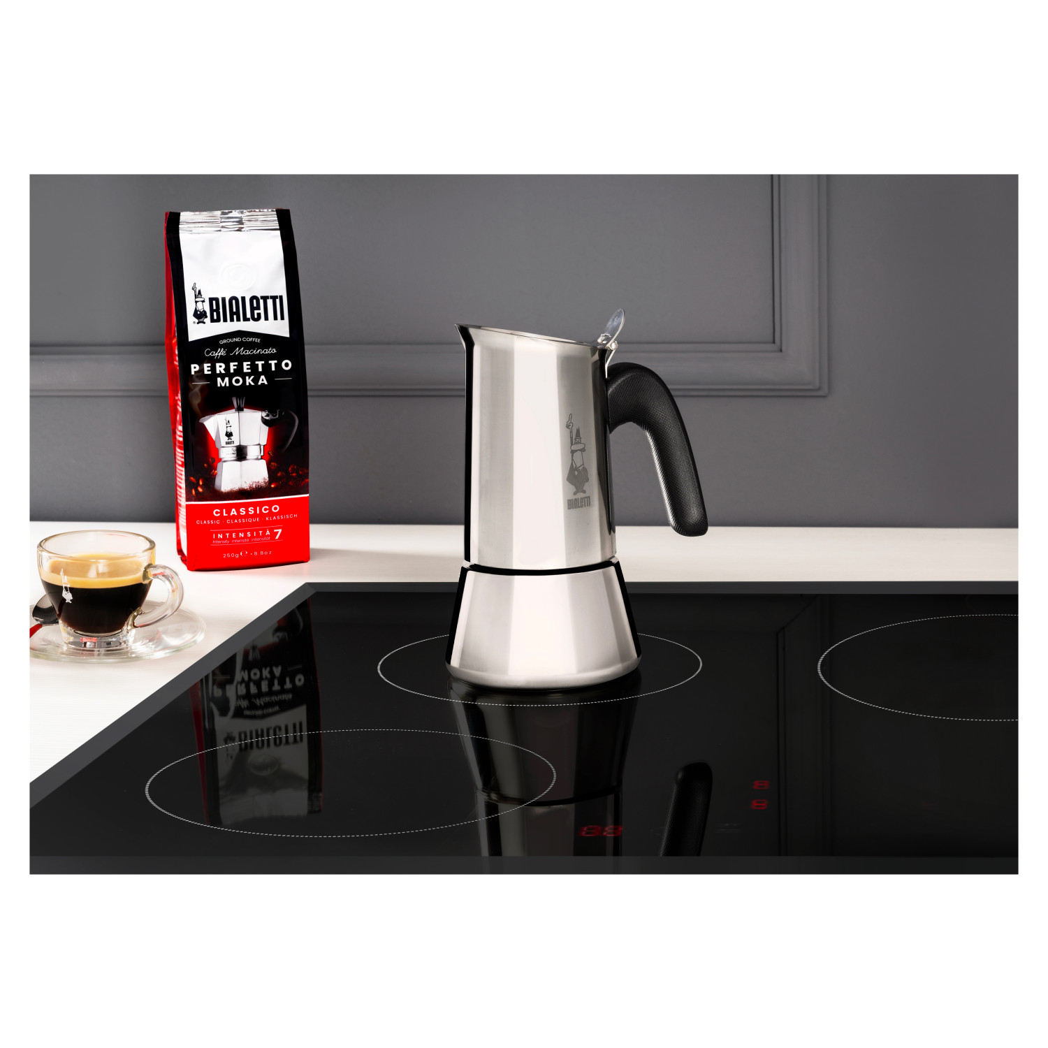 Kawiarka Bialetti Moka na czarnej płycie kuchennej, z torebką kawy i espresso.