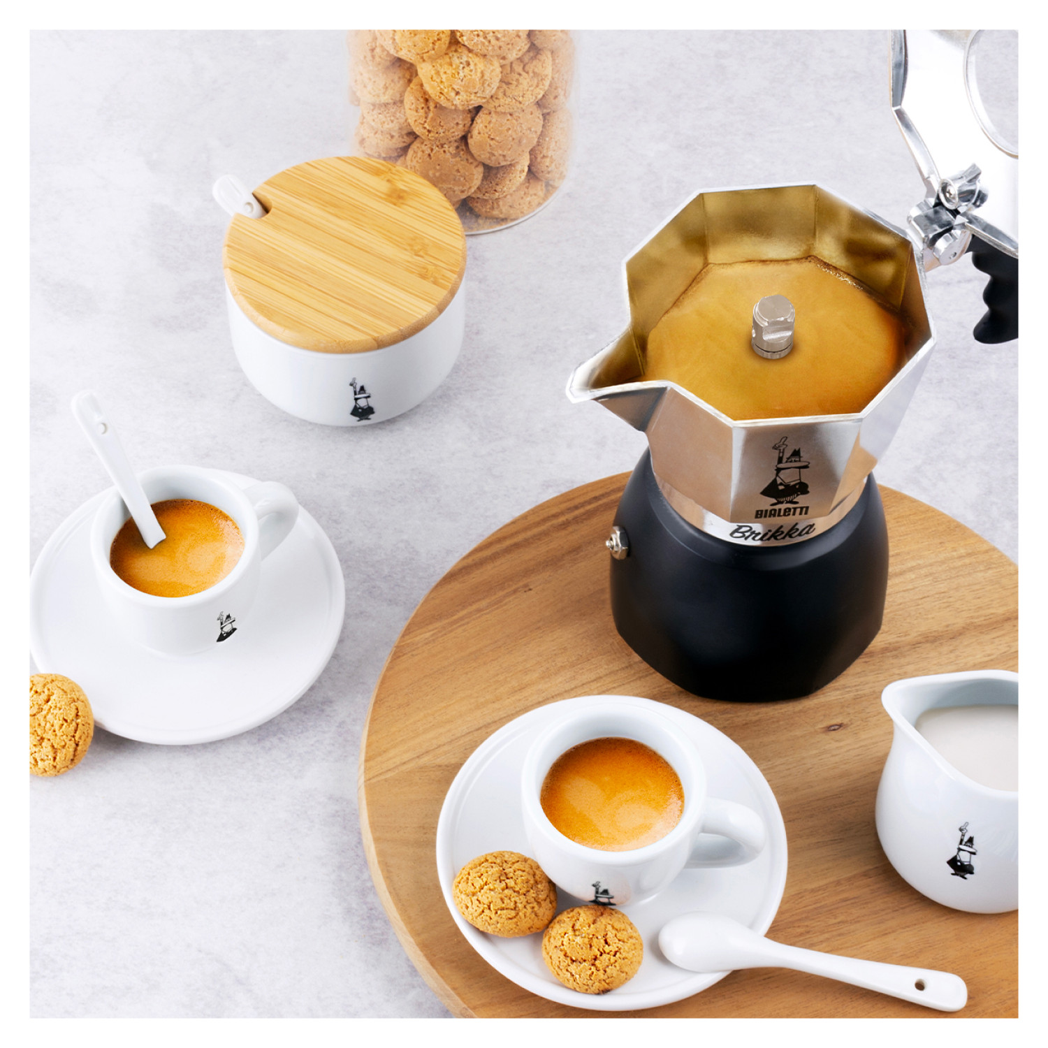 Filiżanki kawy z espresso, ciasteczka i ekspres Bialetti na drewnianej powierzchni.