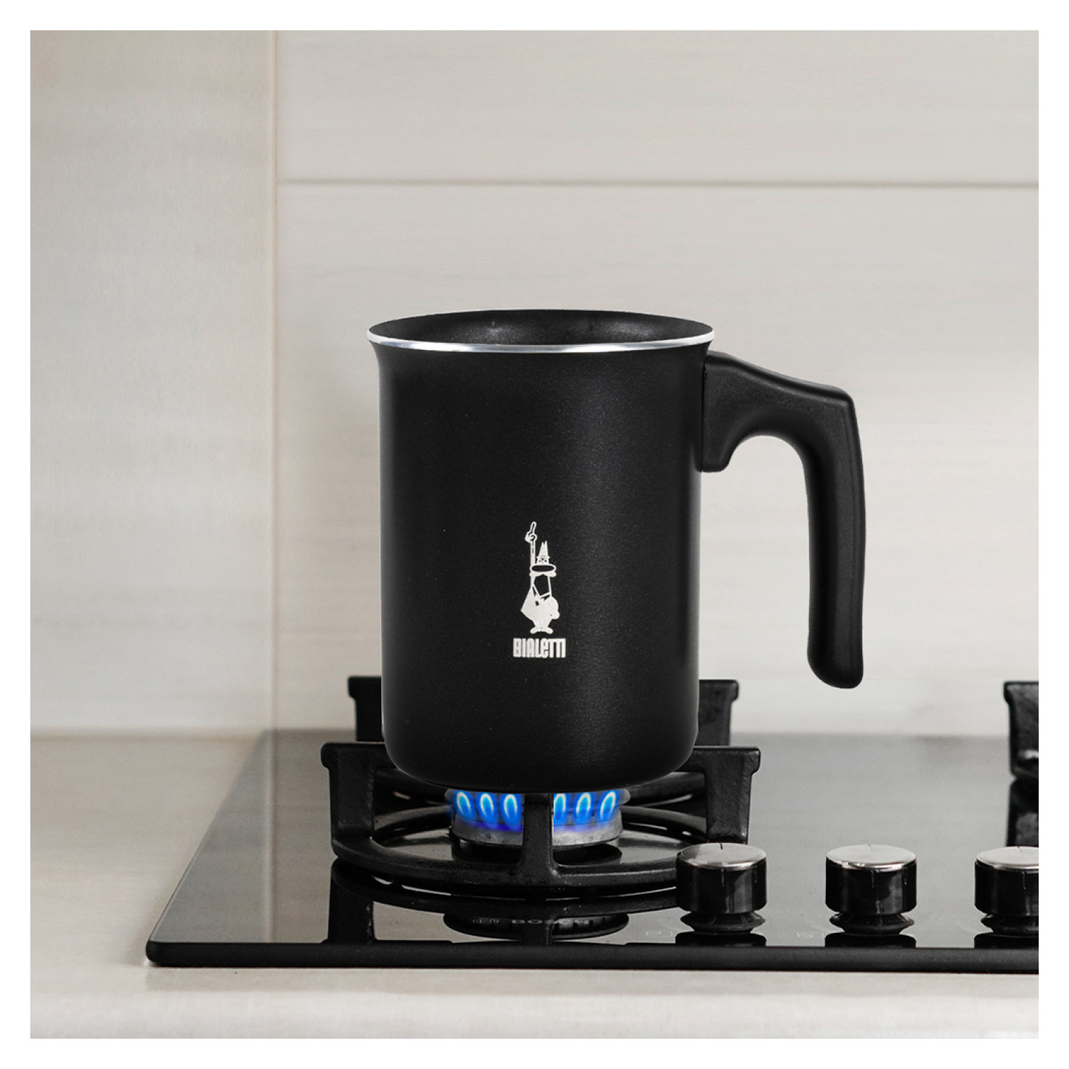 Czarny spieniacz do mleka Bialetti na kuchence. Palnik pod nim jest włączony.