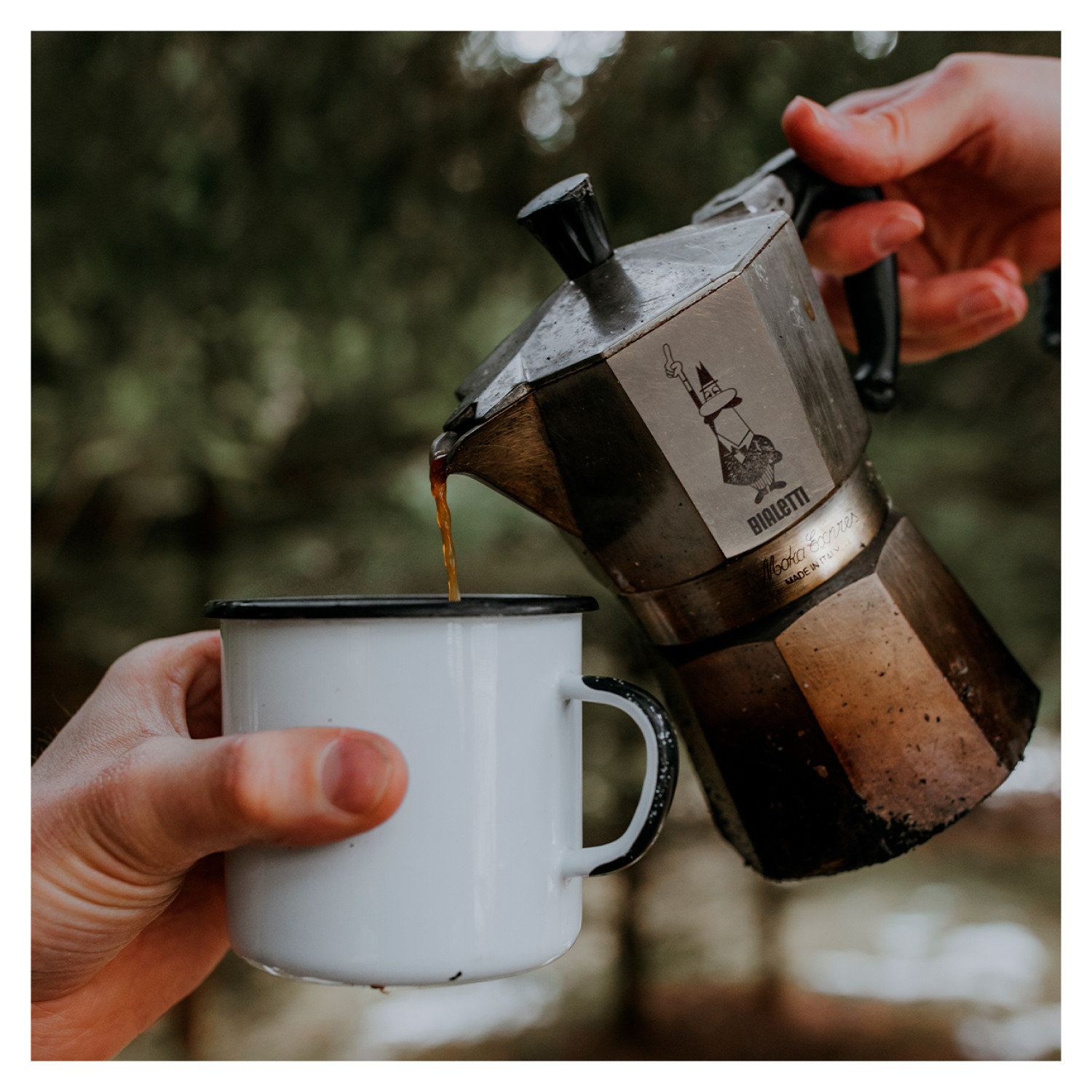 Ręka nalewająca kawę z kawiarki Bialetti Moka do białego kubka. Rozmyte tło.