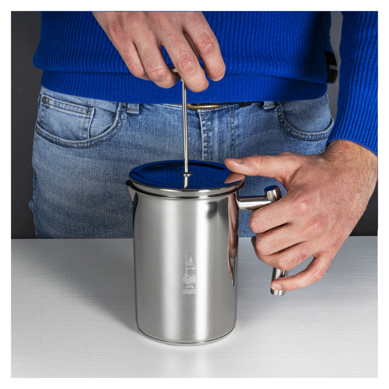 Dłonie używające spieniacza do mleka ze stali nierdzewnej. Niebieska koszula i dżinsy. Biały stół.