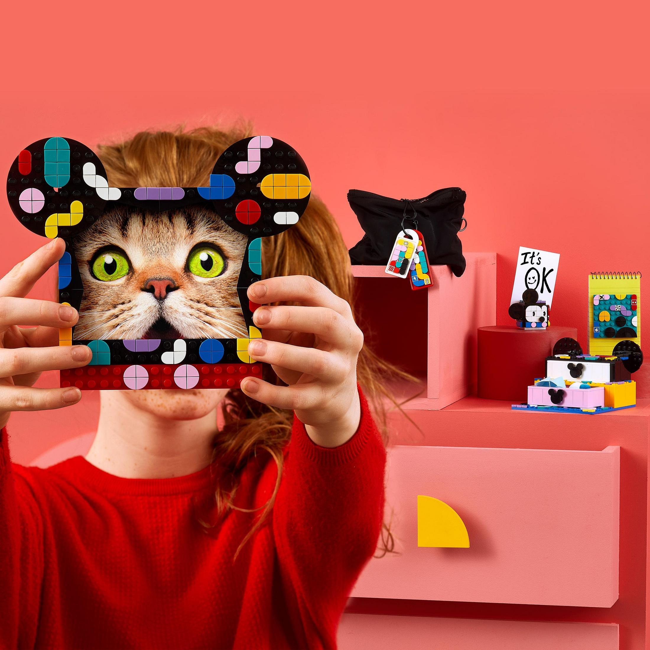 Een kind dat een kattengezicht in Lego-stijl vasthoudt, met andere Lego-modellen in de buurt.