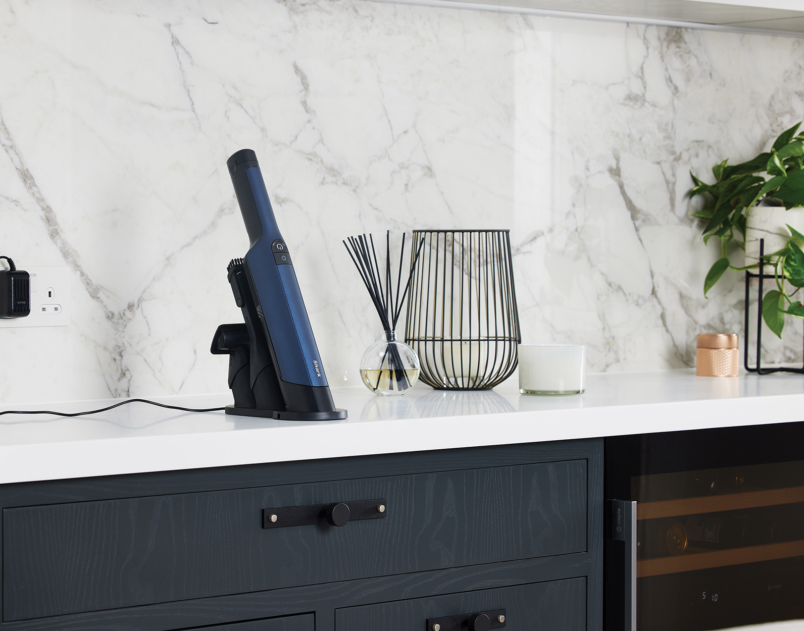 Odkurzacz ręczny w stacji ładującej, na blacie kuchennym obok dekoracji.