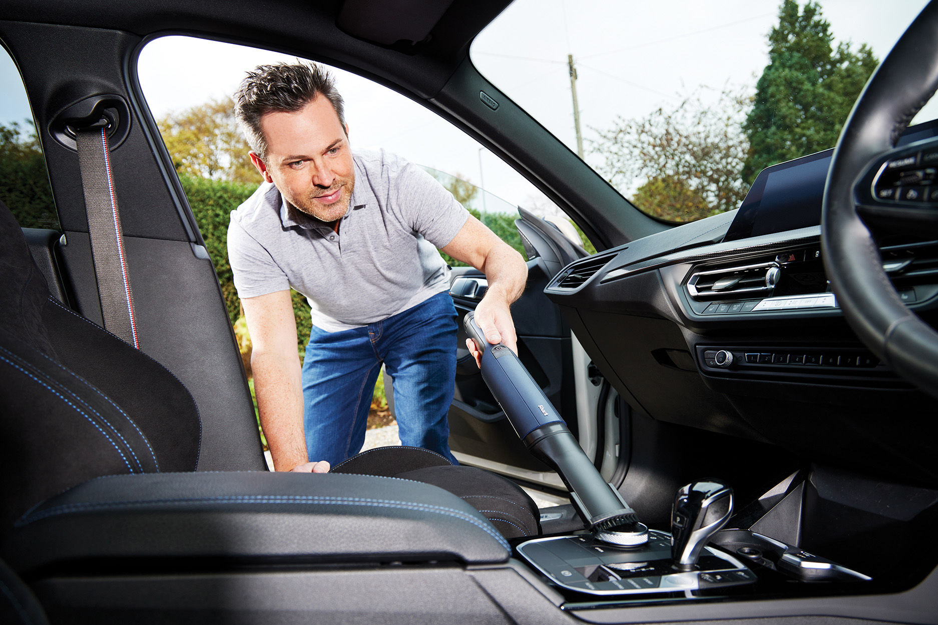 Mężczyzna odkurza wnętrze samochodu za pomocą odkurzacza ręcznego.