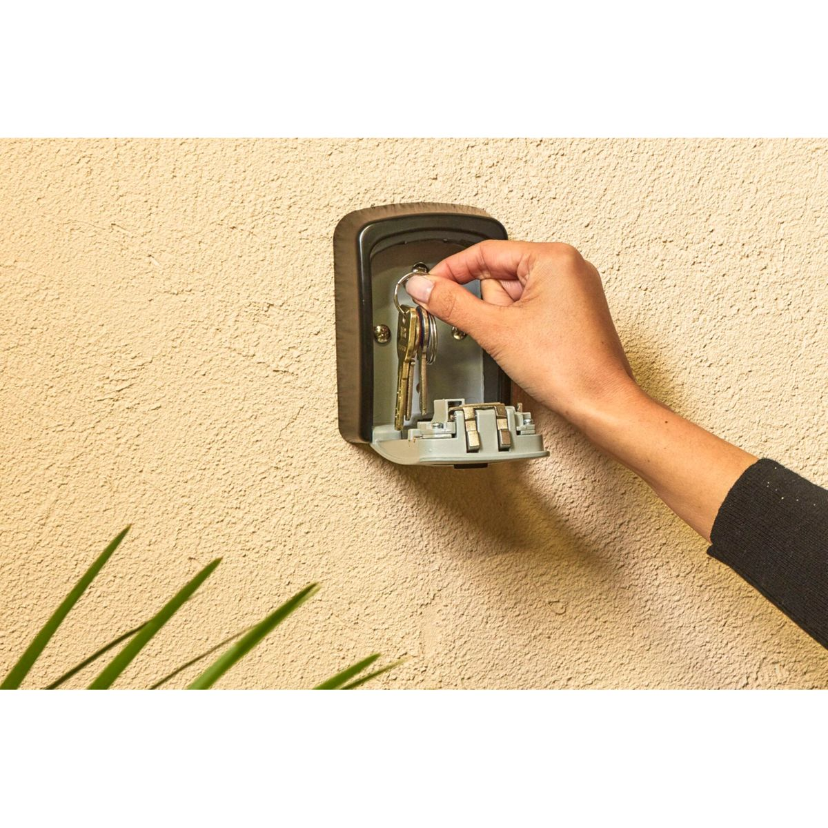 Mano che apre una cassaforte per chiavi su un muro beige strutturato. Cassaforte marrone.