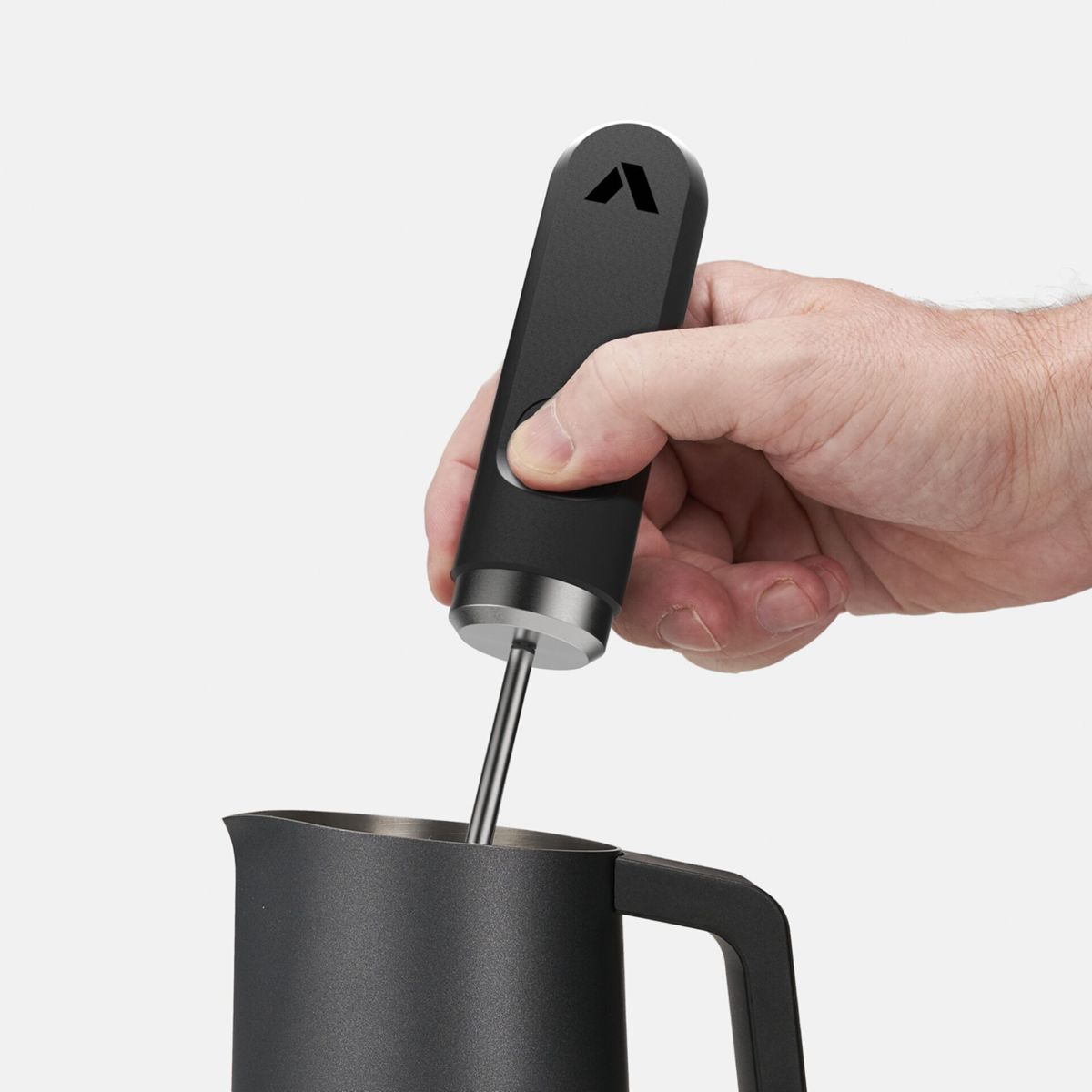 Eine Hand hält ein schwarzes Aufschäumwerkzeug und einen schwarzen Krug.