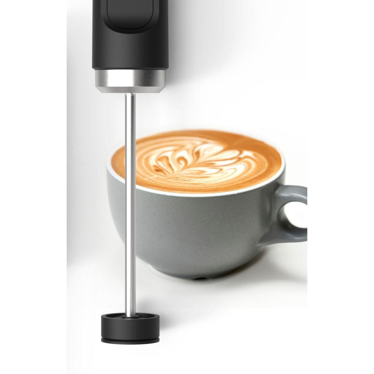 Milchaufschäumer über einer Kaffeetasse mit Latte Art. Graue Tasse und weißer Hintergrund.