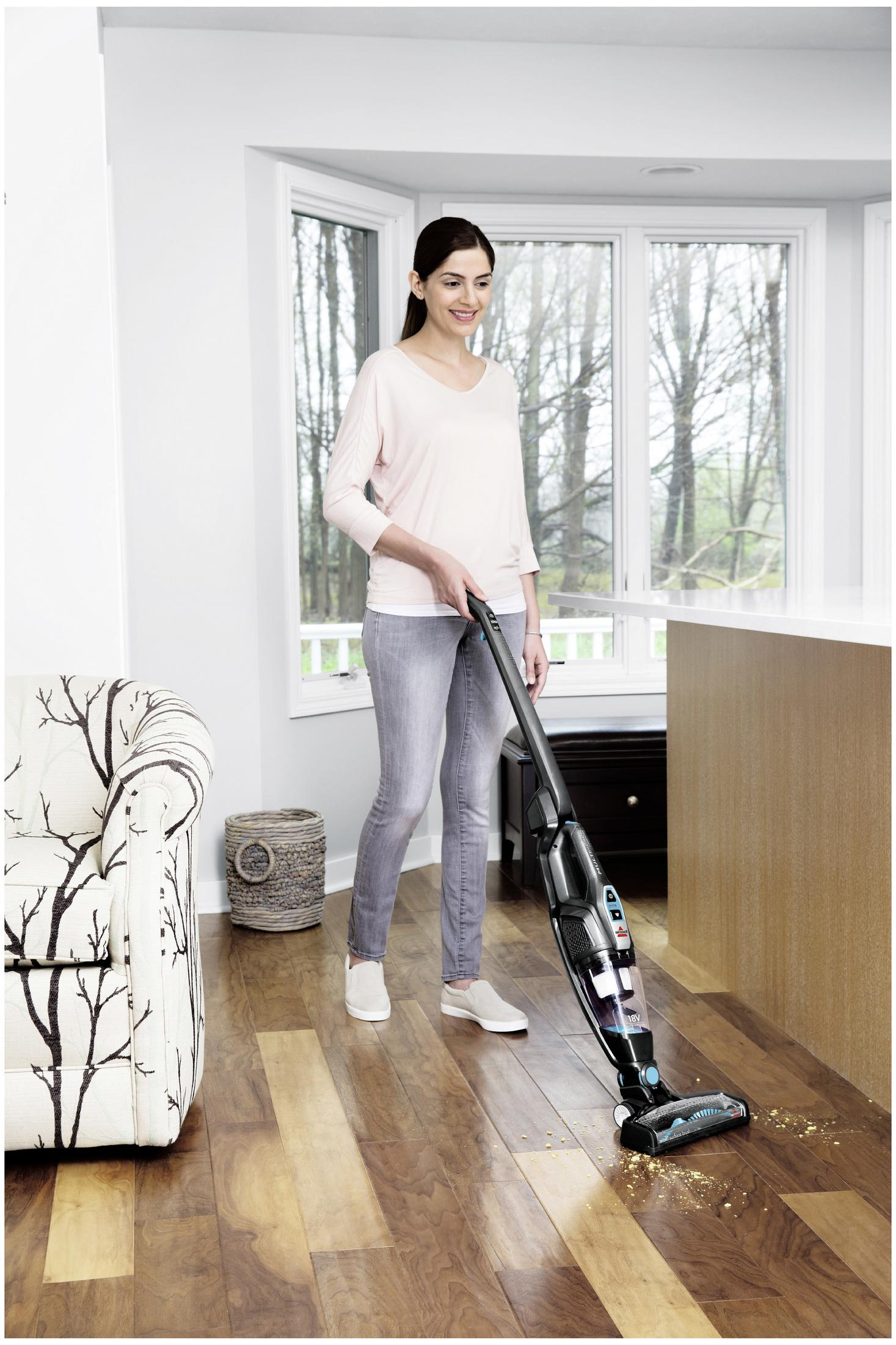 Kobieta odkurzająca drewnianą podłogę w jasnym pokoju odkurzaczem.