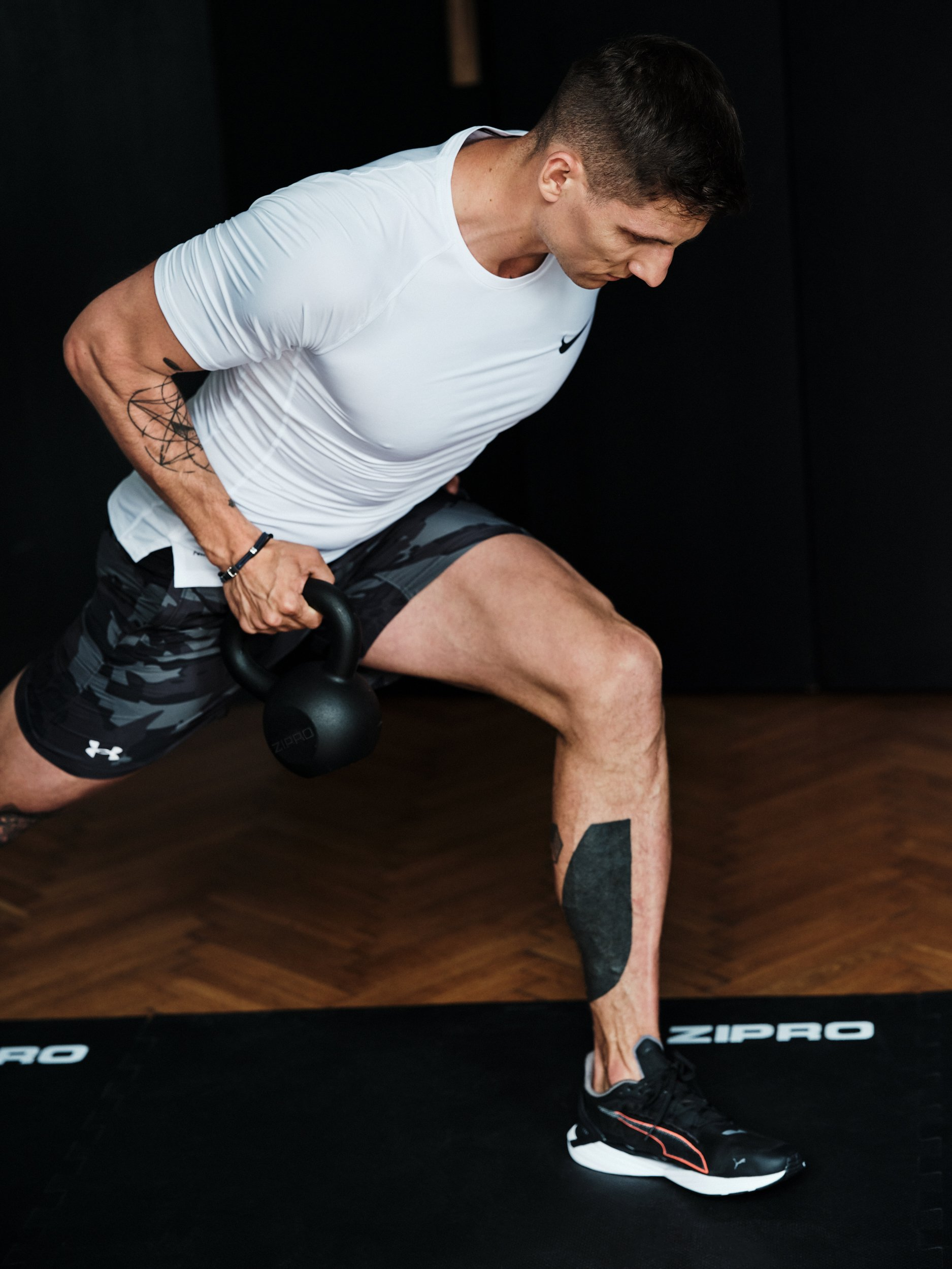 Mann, der mit einer Kettlebell trainiert, trägt ein weißes Hemd und Shorts.