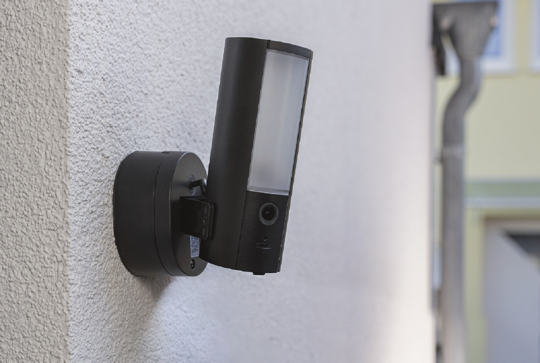 Schwarze Überwachungskamera an einer weißen Wand montiert. Die Kamera ist angewinkelt und hat ein Licht.