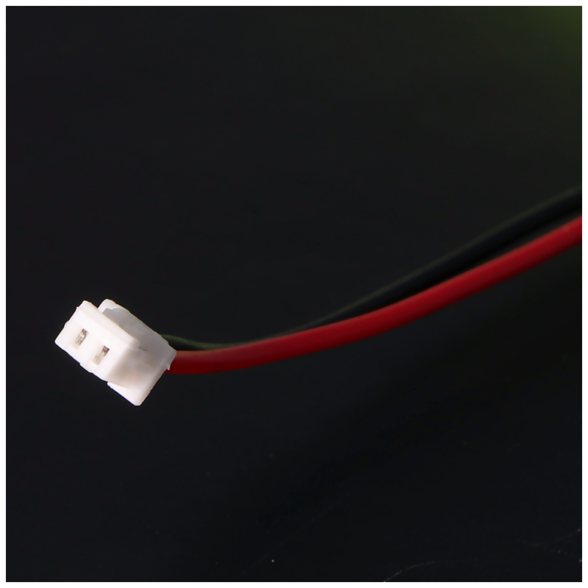 Ein weißer Stecker mit zwei Drähten: ein roter und ein schwarzer, auf weißem Hintergrund.