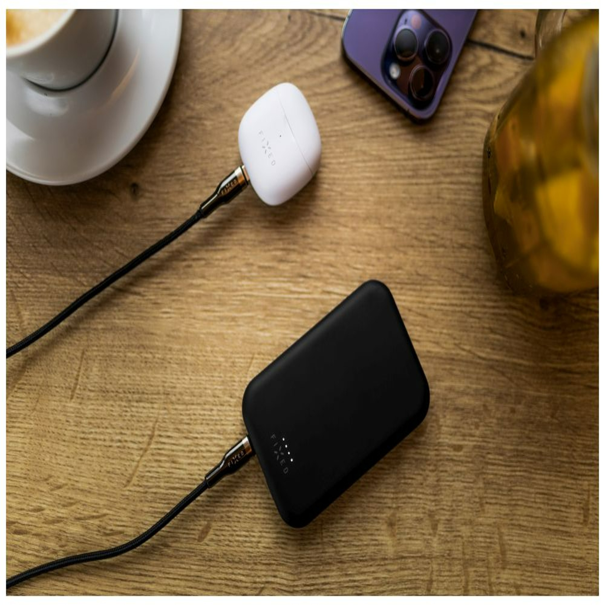 Eine schwarze Powerbank, verbunden mit weißen Ohrhörern und einem Telefon, auf Holz.