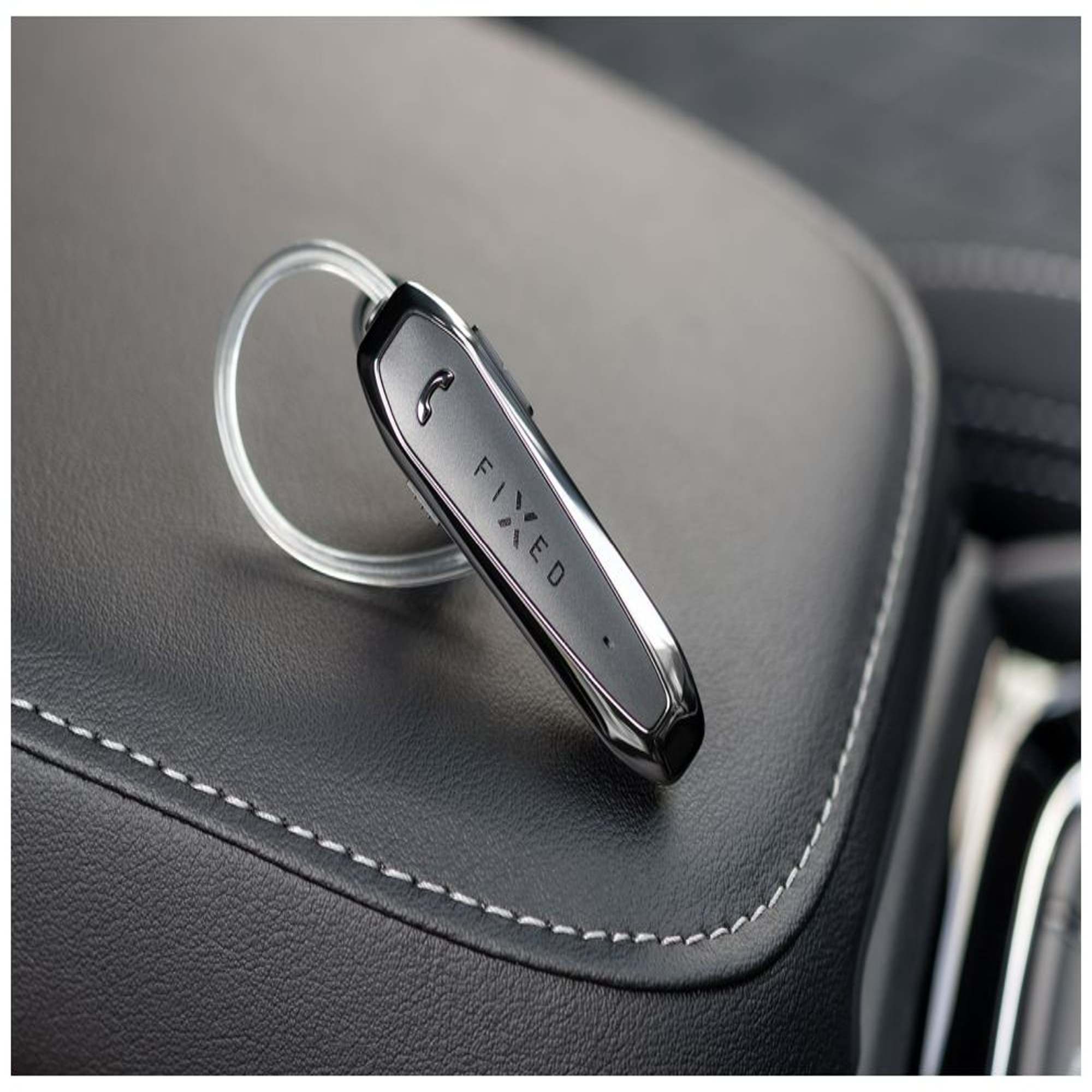 Ein schwarzes Bluetooth-Headset auf einem schwarzen Ledersitz mit weißen Nähten.
