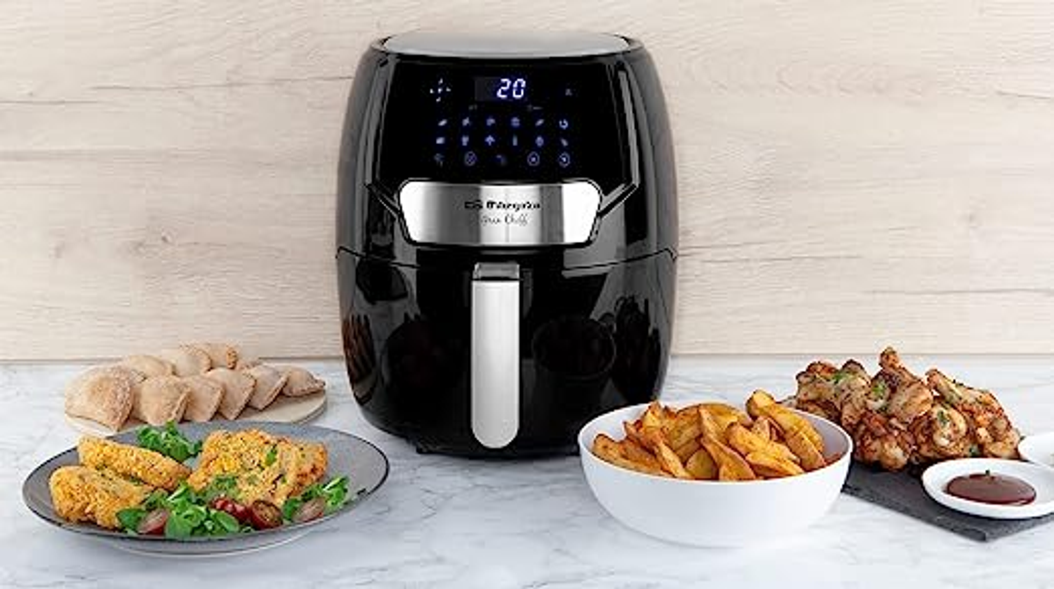 Czarna frytkownica powietrzna z smażonym jedzeniem i składnikami na drewnianej powierzchni. Wyświetla cyfrowe sterowanie.