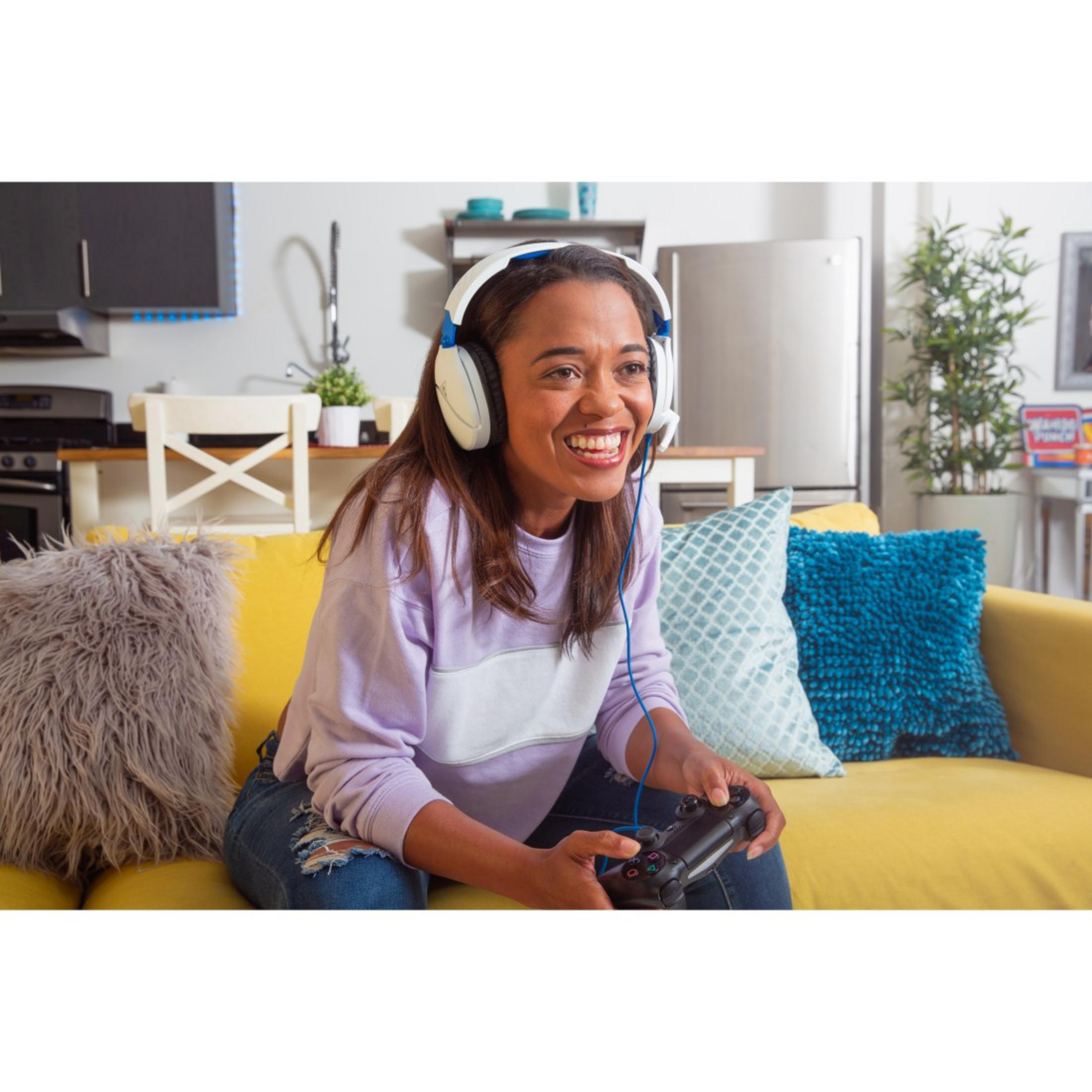 Kobieta grająca na żółtej kanapie, w słuchawkach i trzymająca kontroler.