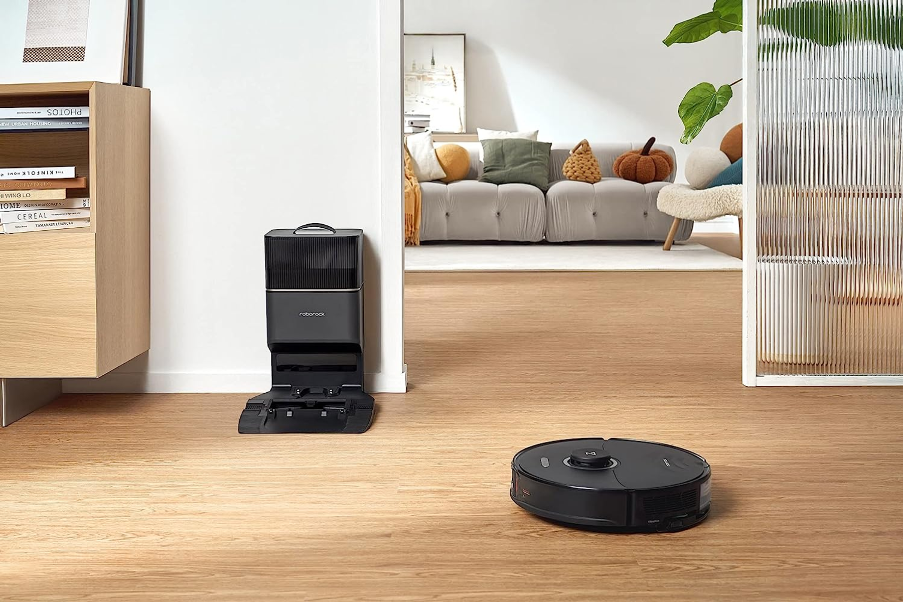 Czarny robot odkurzający na drewnianej podłodze, obok stacji dokującej.