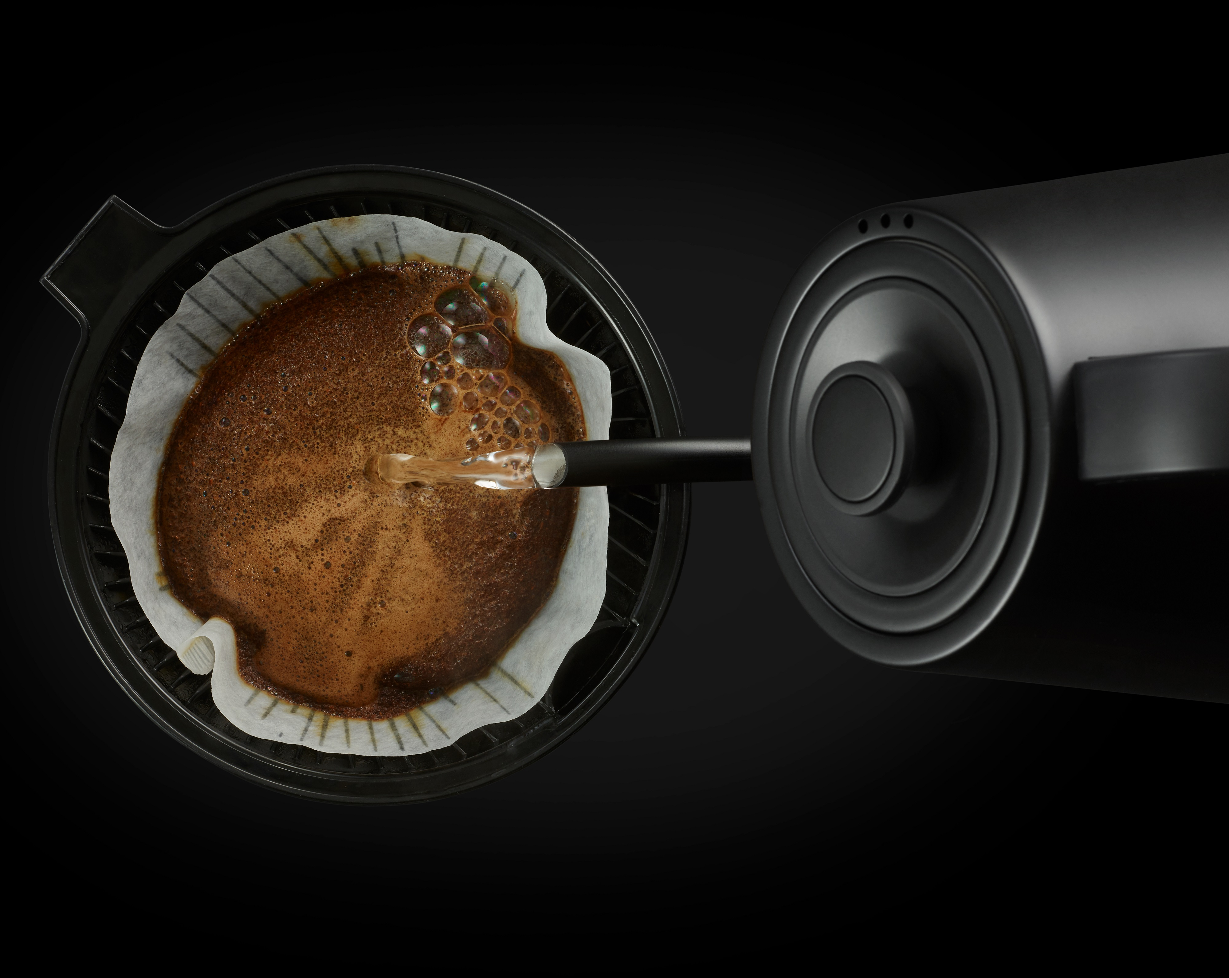 Kaffee wird in einen Filter mit Kaffeesatz gegossen, schwarzer Hintergrund.
