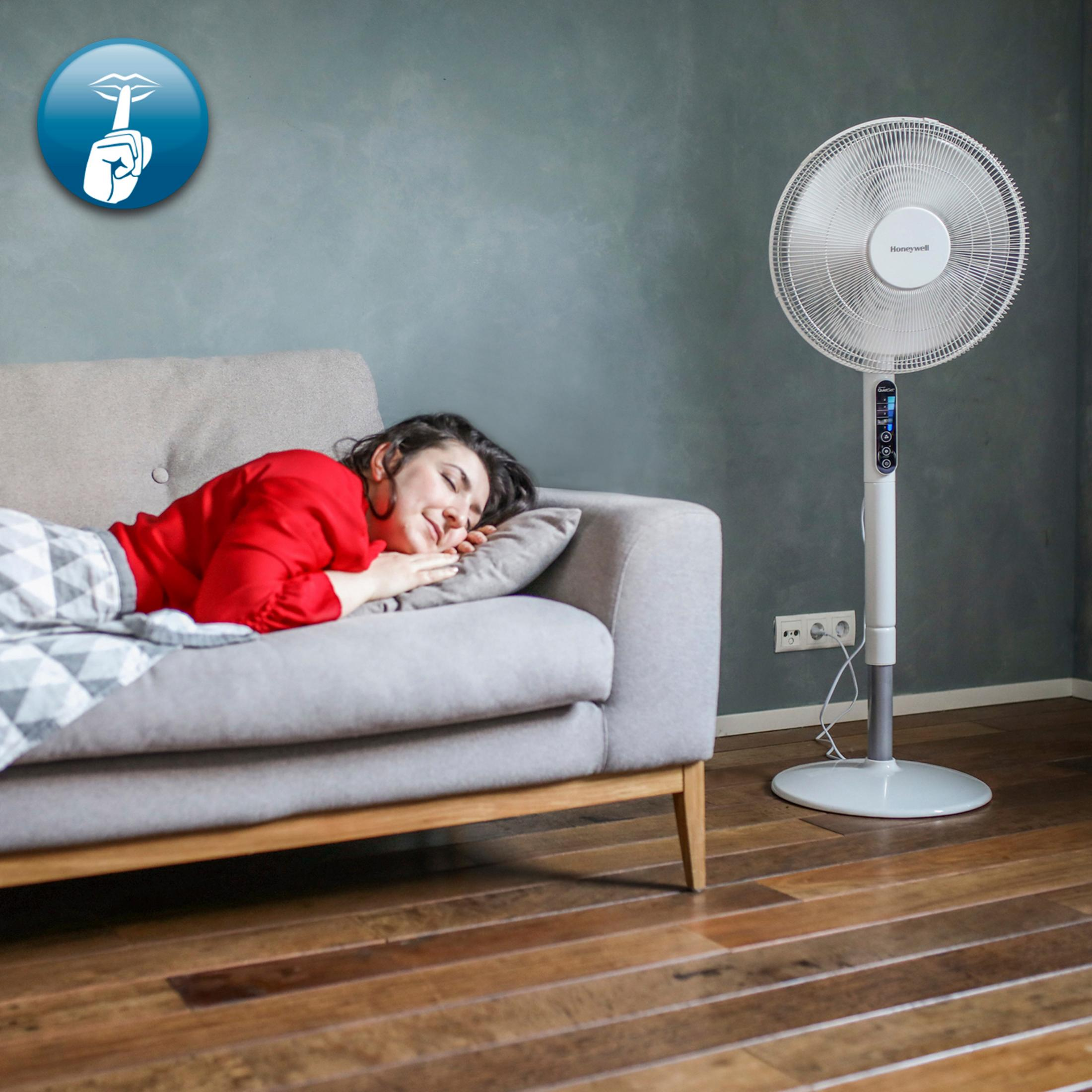 Kobieta śpi na kanapie obok wentylatora stojącego w pokoju z drewnianą podłogą.