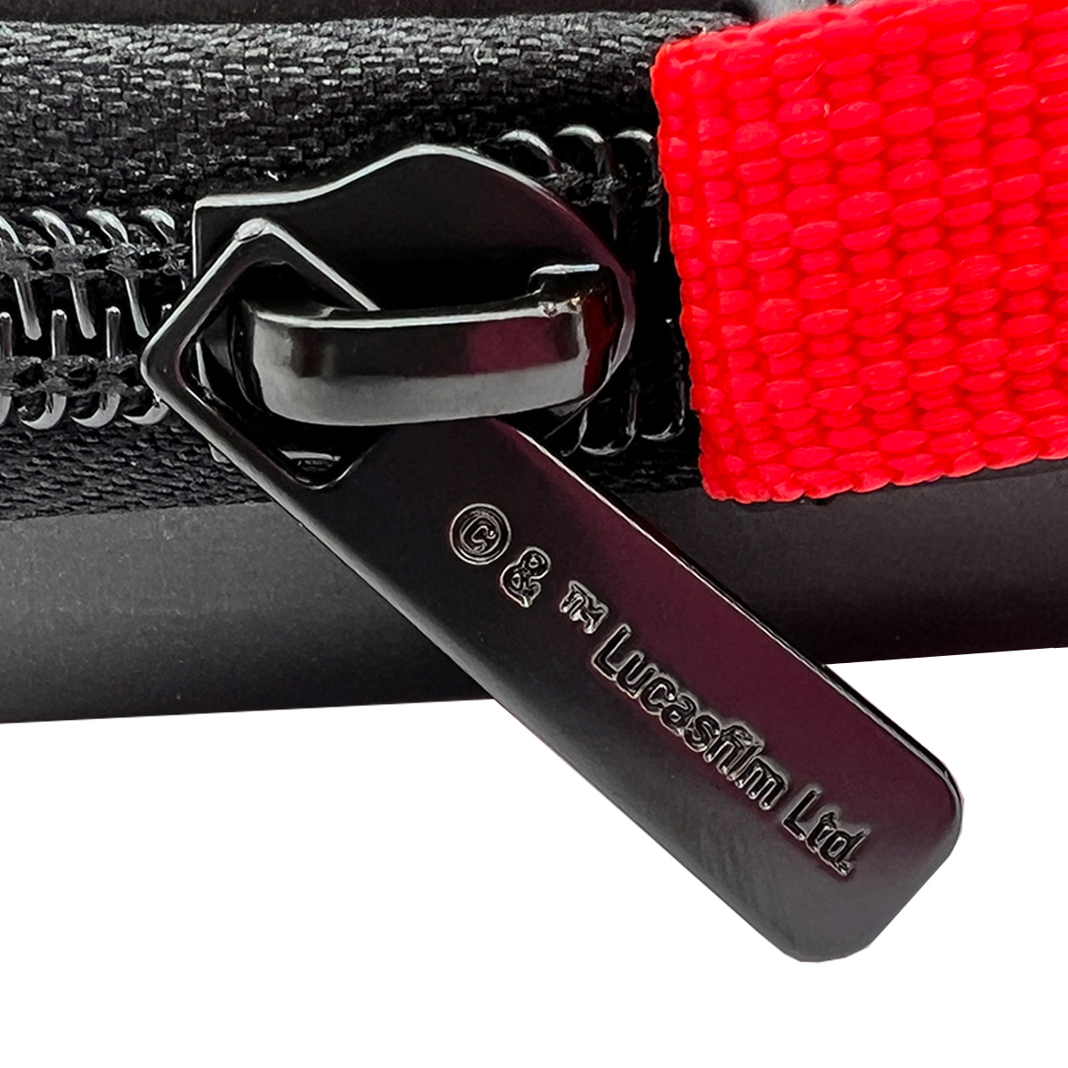 Tirador de cremallera negro con marca Lucasfilm Ltd. Tejido rojo.