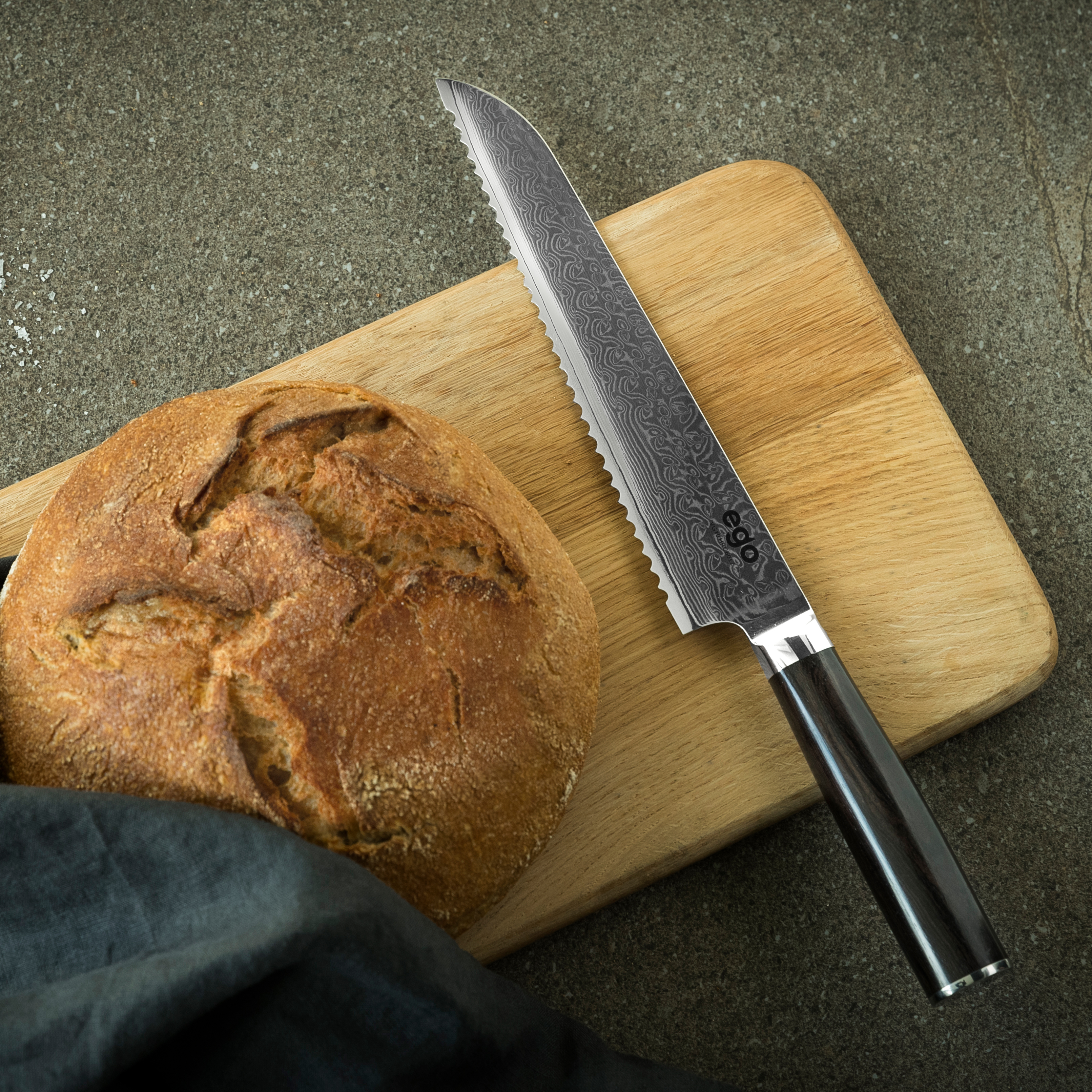 Ein Messer liegt auf einem Holzbrett neben einem Brotlaib, beides auf einer grauen Oberfläche.