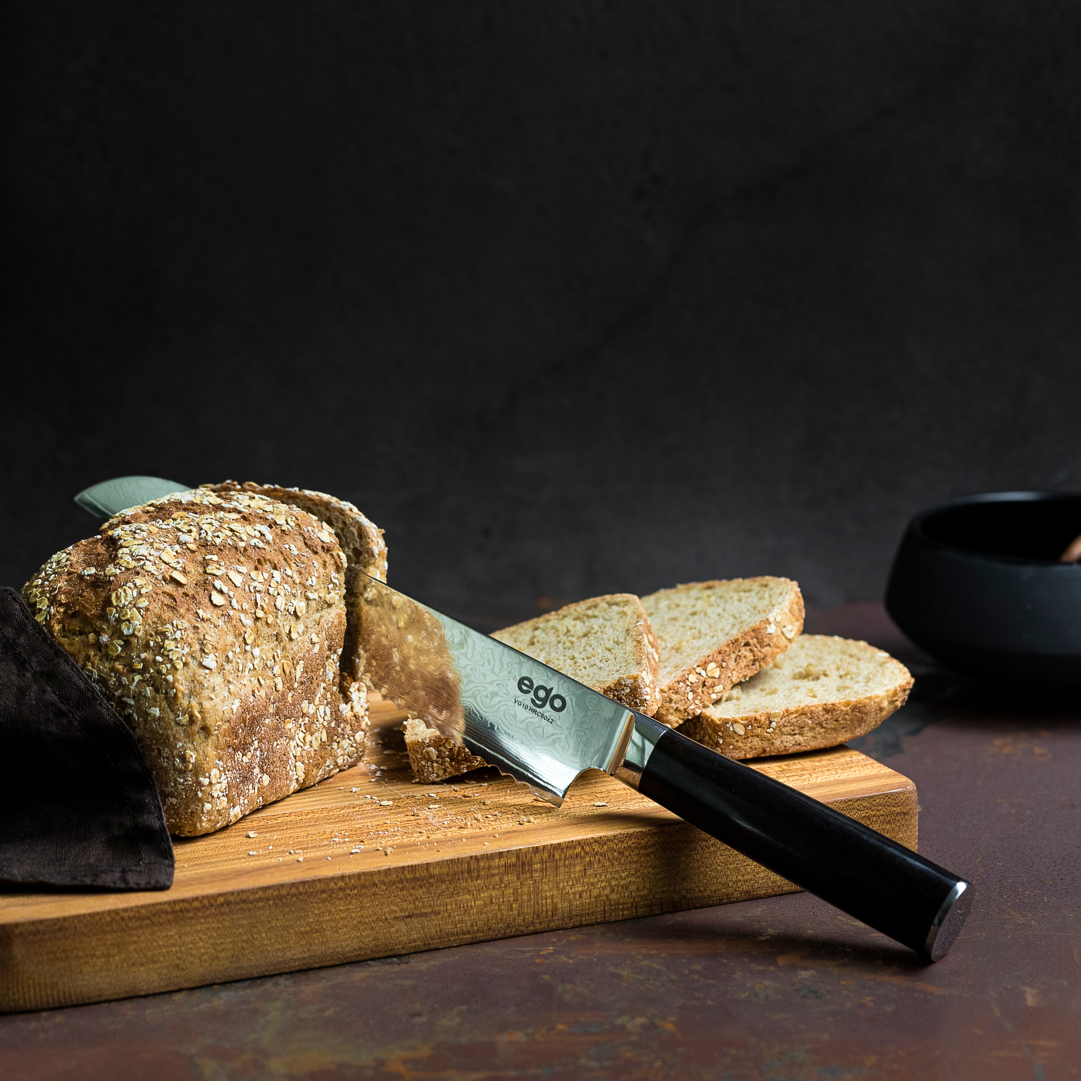 Brot wird mit einem Messer geschnitten. Das Messer hat einen schwarzen Griff. Holz- und dunkler Hintergrund.