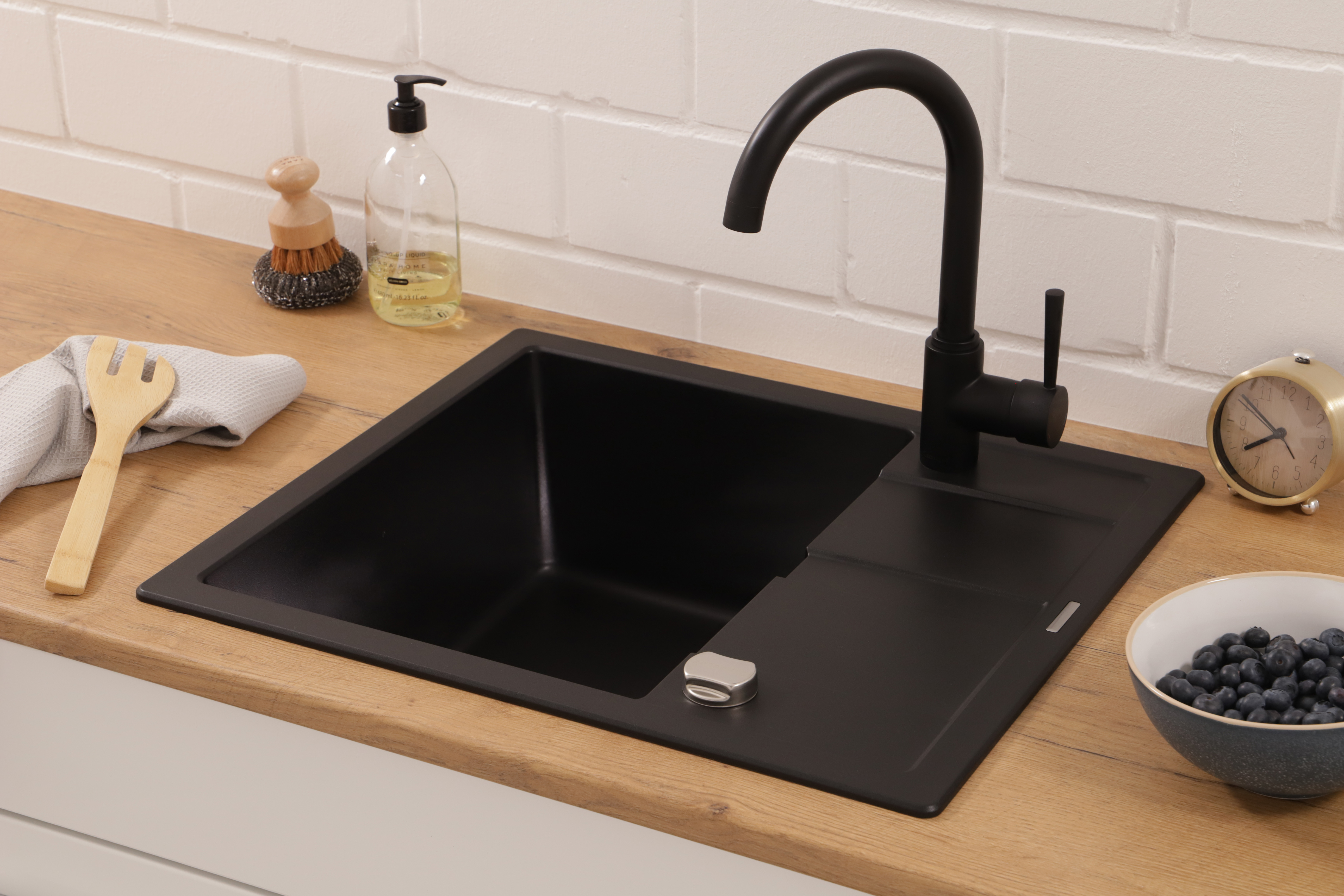 Lavello e rubinetto da cucina neri su un piano di lavoro in legno. Sapone, spazzola e mirtilli accanto.