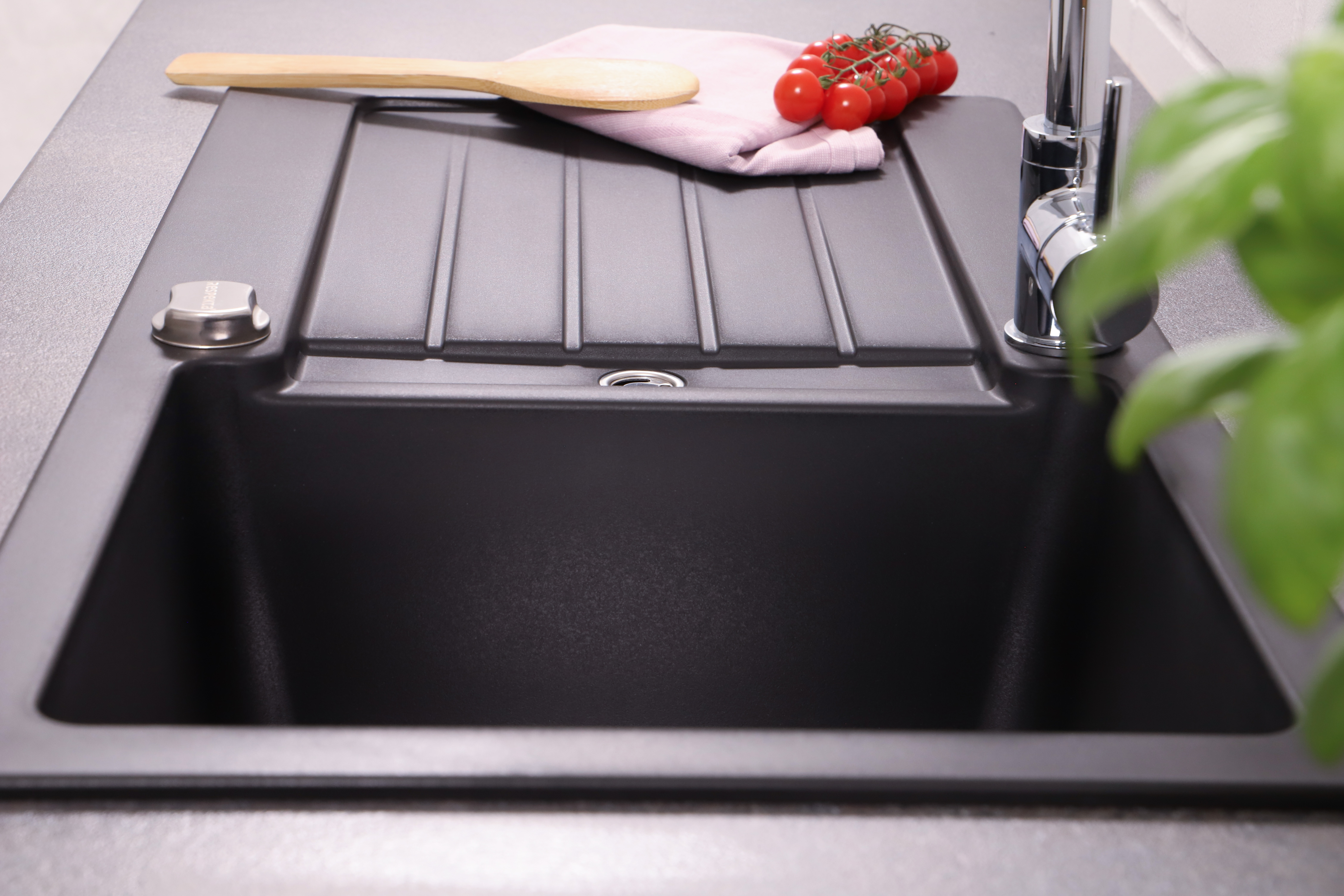 Schwarzes Küchenbecken mit einem Holzlöffel, Tomaten und einem rosa Handtuch.