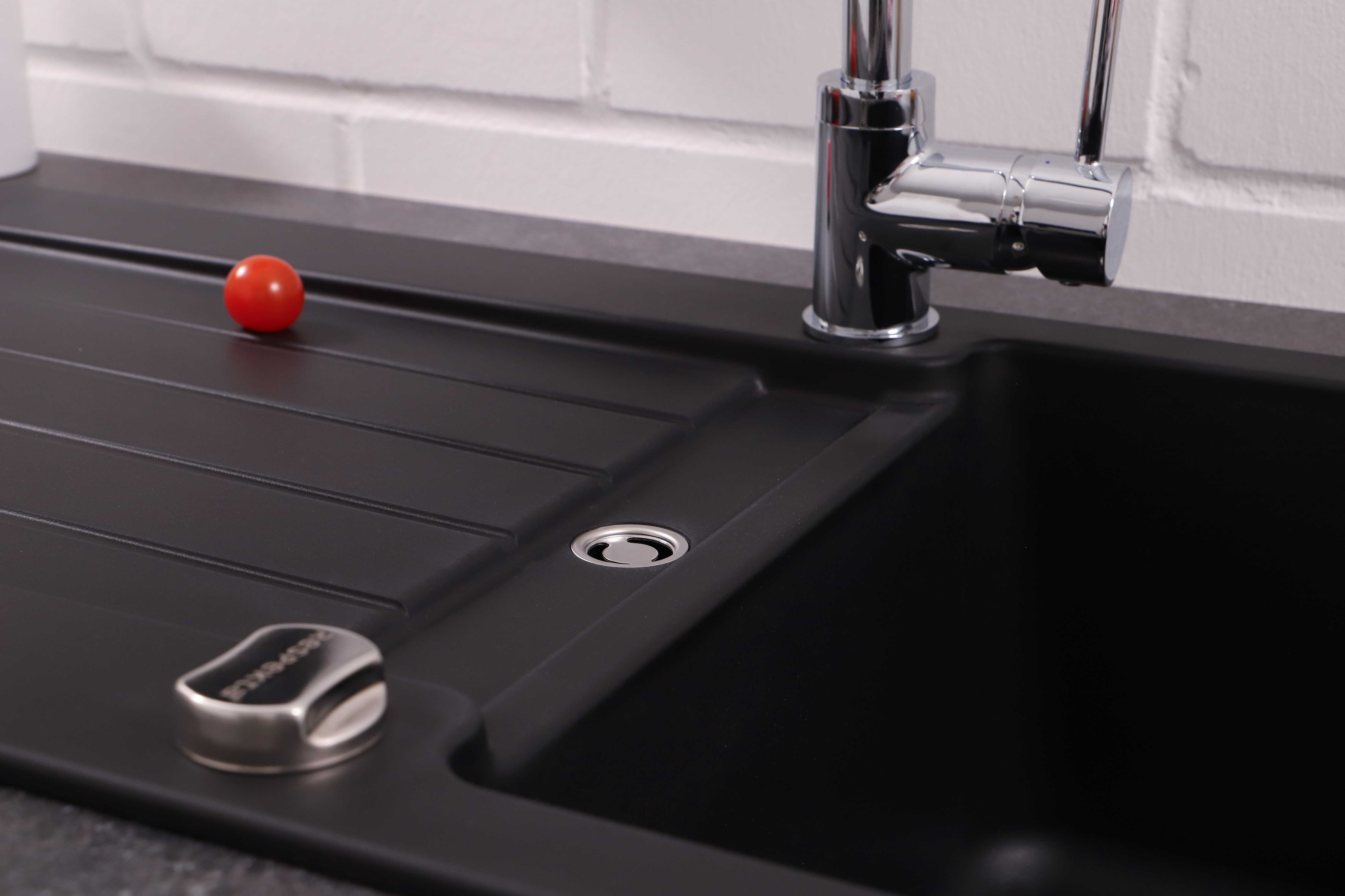 Schwarzes Küchenbecken mit Wasserhahn, Tomate und Seifenspender.