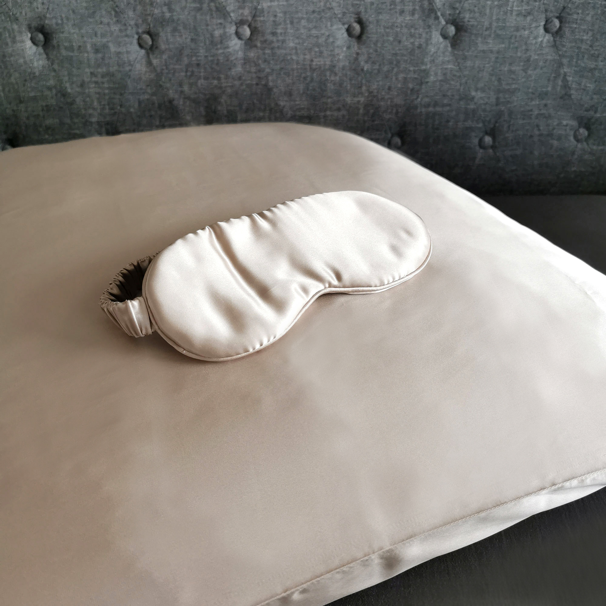 Beiges Kissen mit passender Augenmaske. Graues Sofa.