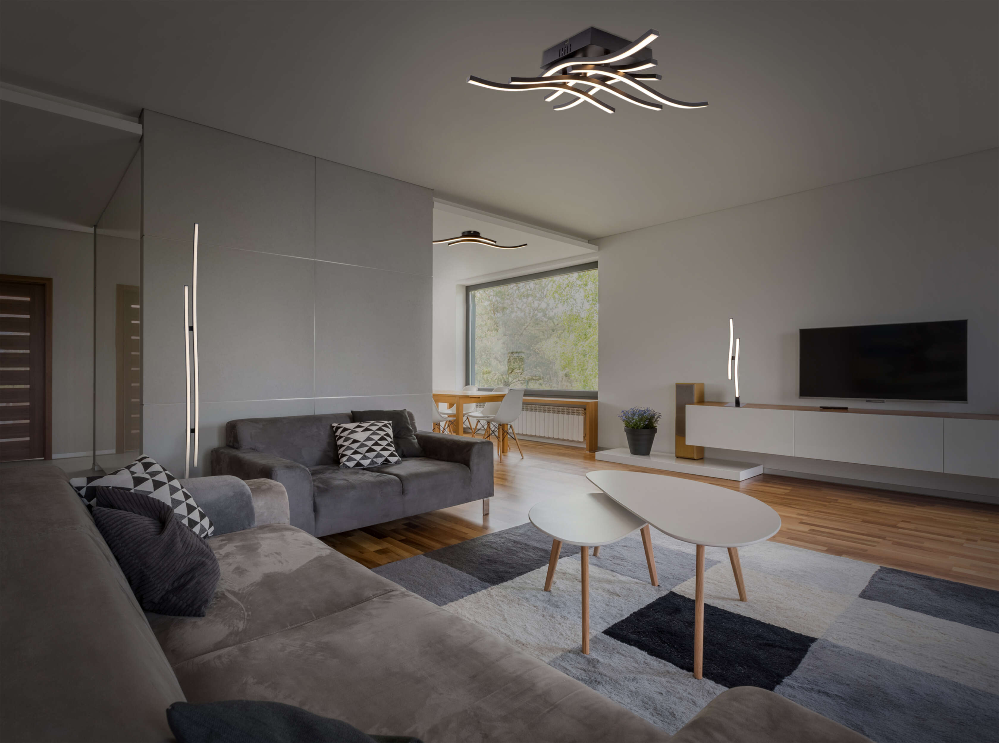 Modernes Wohnzimmer mit grauem Sofa, zwei Lampen und Deckenbeleuchtung.