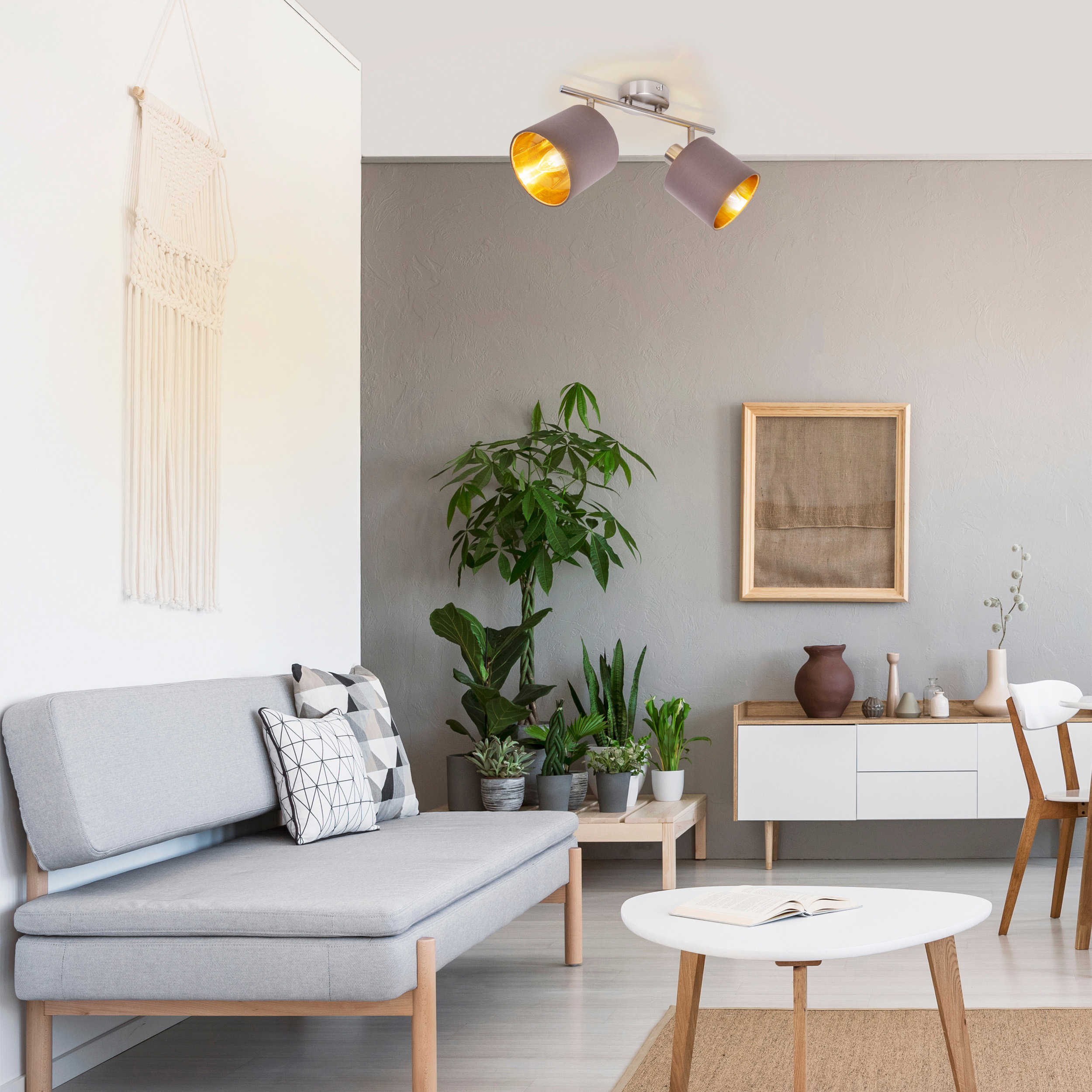 Wohnzimmer mit Pflanzen, weißem Sofa und Couchtisch. Deckenleuchten.