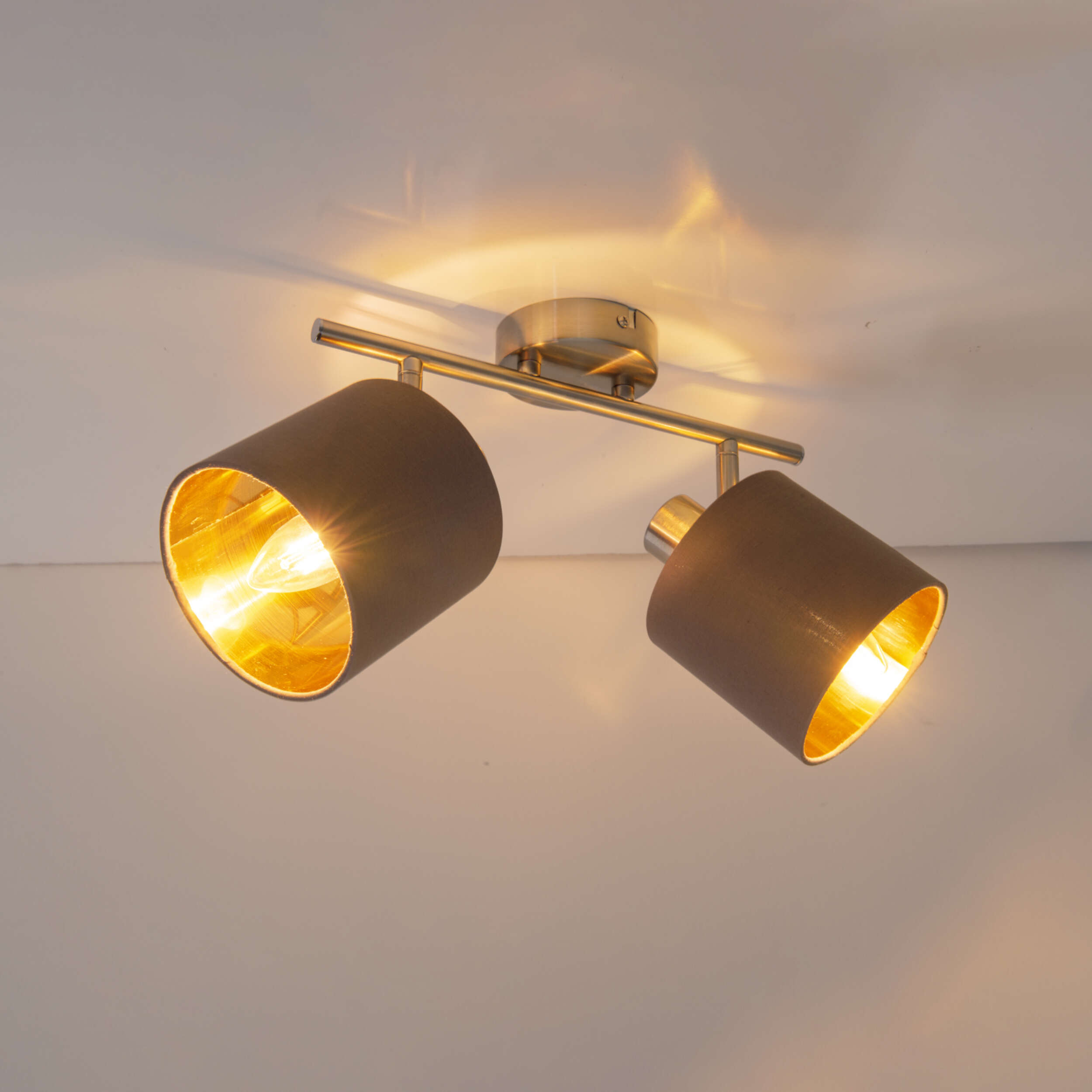 Zwei Strahler mit goldenem Innenraum sind auf einem Metallbügel an einer weißen Decke montiert.