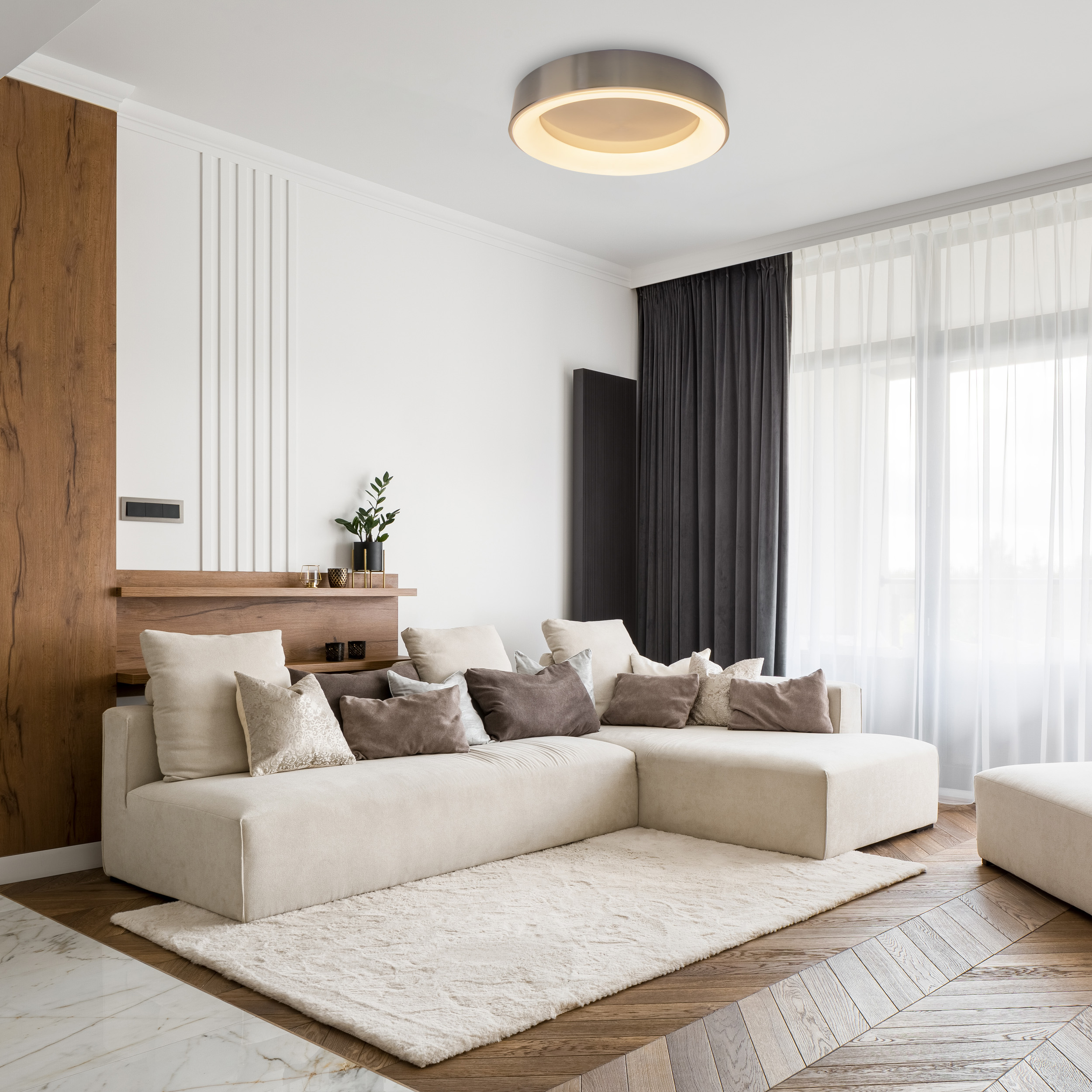 Wohnzimmer mit beigem Sofa, weißen Wänden, Holzböden und runder Deckenleuchte.