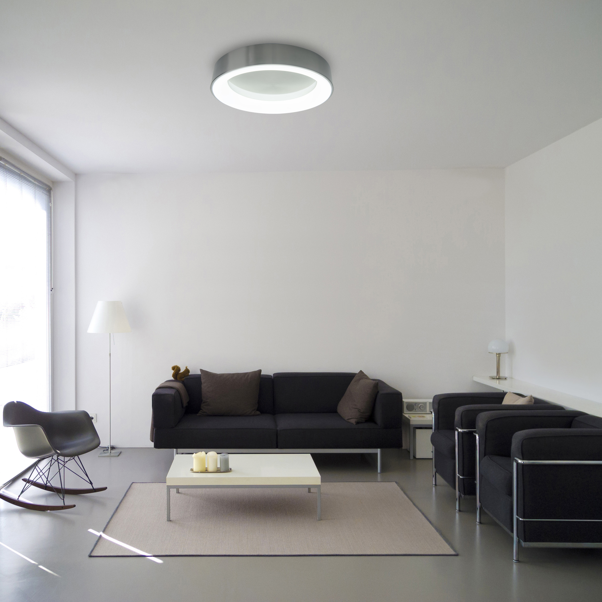 Ein Wohnzimmer mit Sofa, Stühlen, Couchtisch, Teppich und Deckenleuchte.