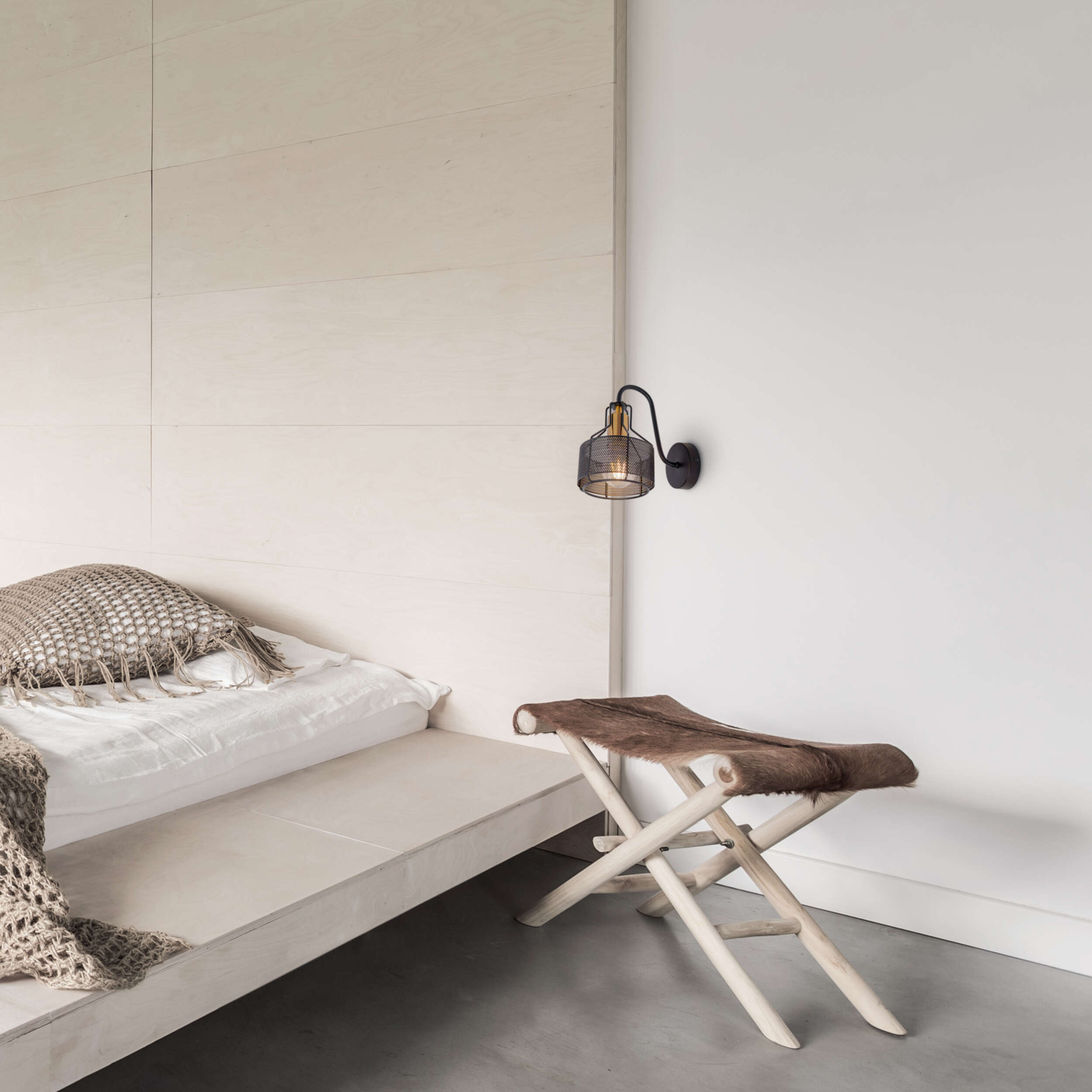 Schlafzimmer mit Bett und Kissen, Holzschemel mit Fell und Wandlampe.