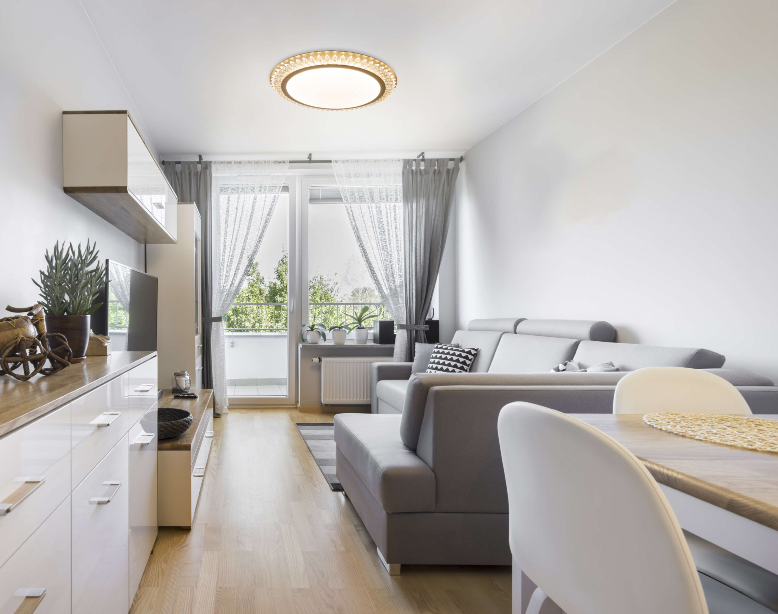 Wohnzimmer mit weißen Wänden, grauem Sofa und Lampe. Es gibt eine Balkontür.