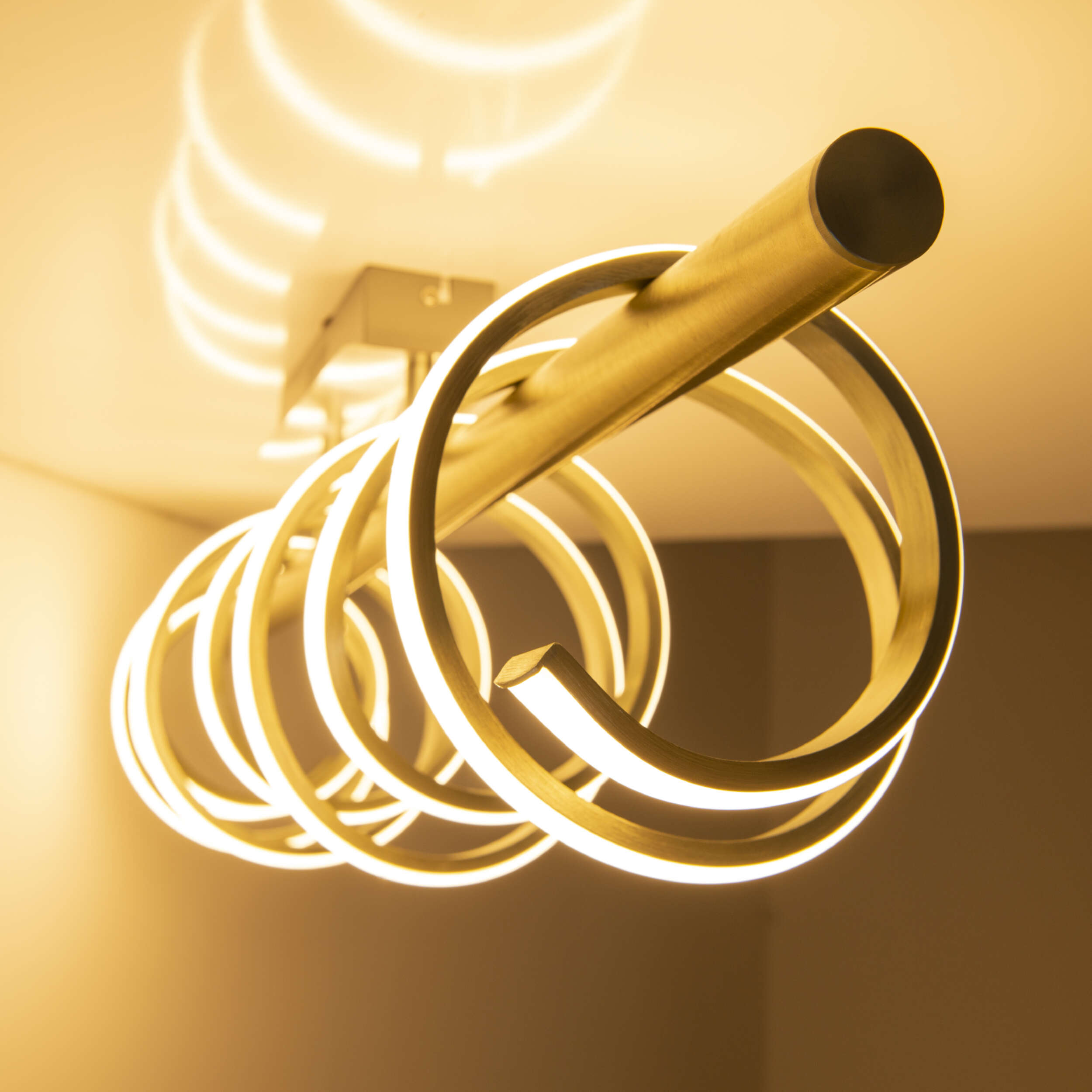 Deckenlampe mit mehreren leuchtenden Ringen in einem Raum mit hellfarbiger Wand.