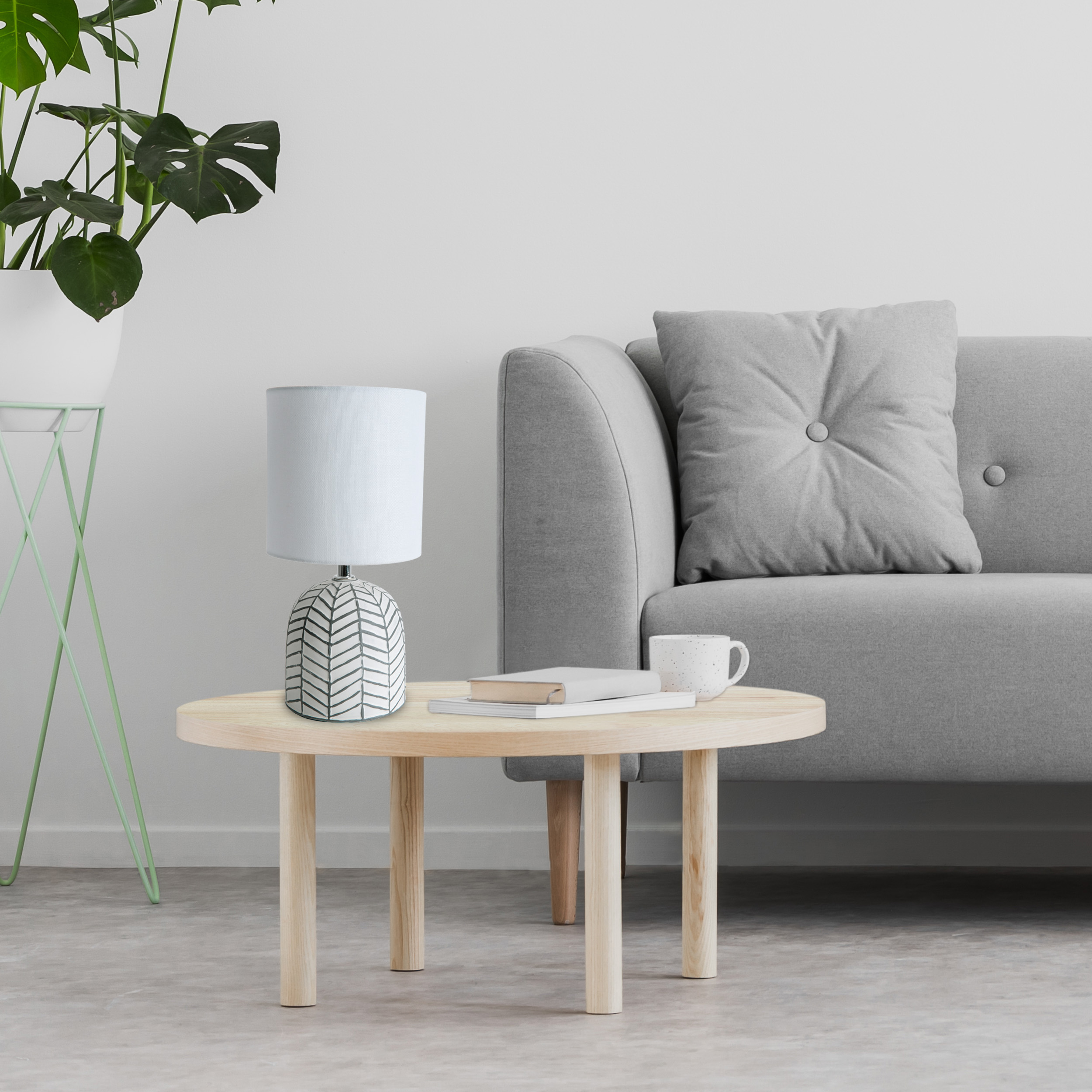 Eine Tischlampe auf einem Holztisch neben einem grauen Sofa und einer Pflanze in einem weißen Topf.