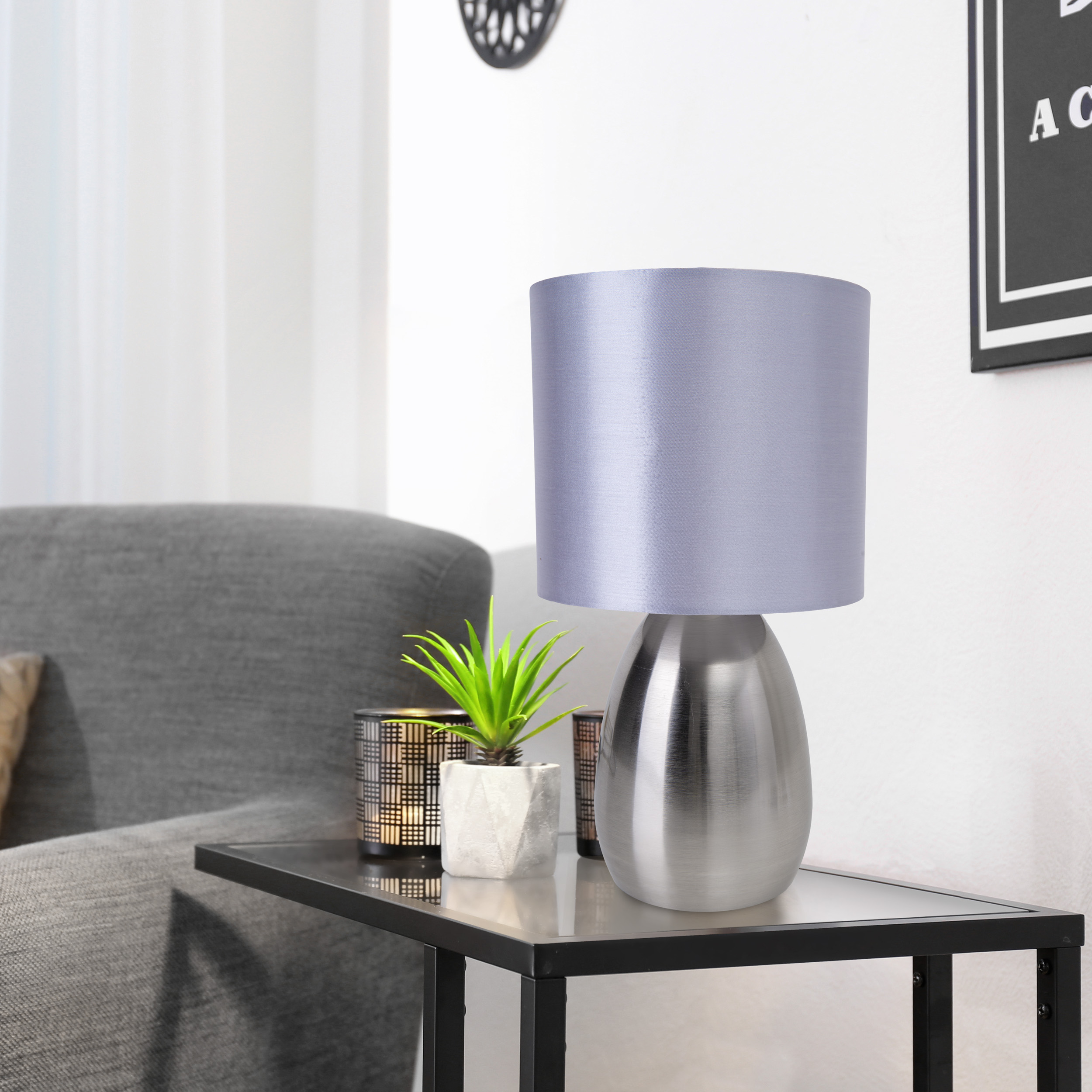 Silberne Tischlampe mit grauem Schirm auf einem schwarzen Tisch. Kleine Pflanze und Dekor.