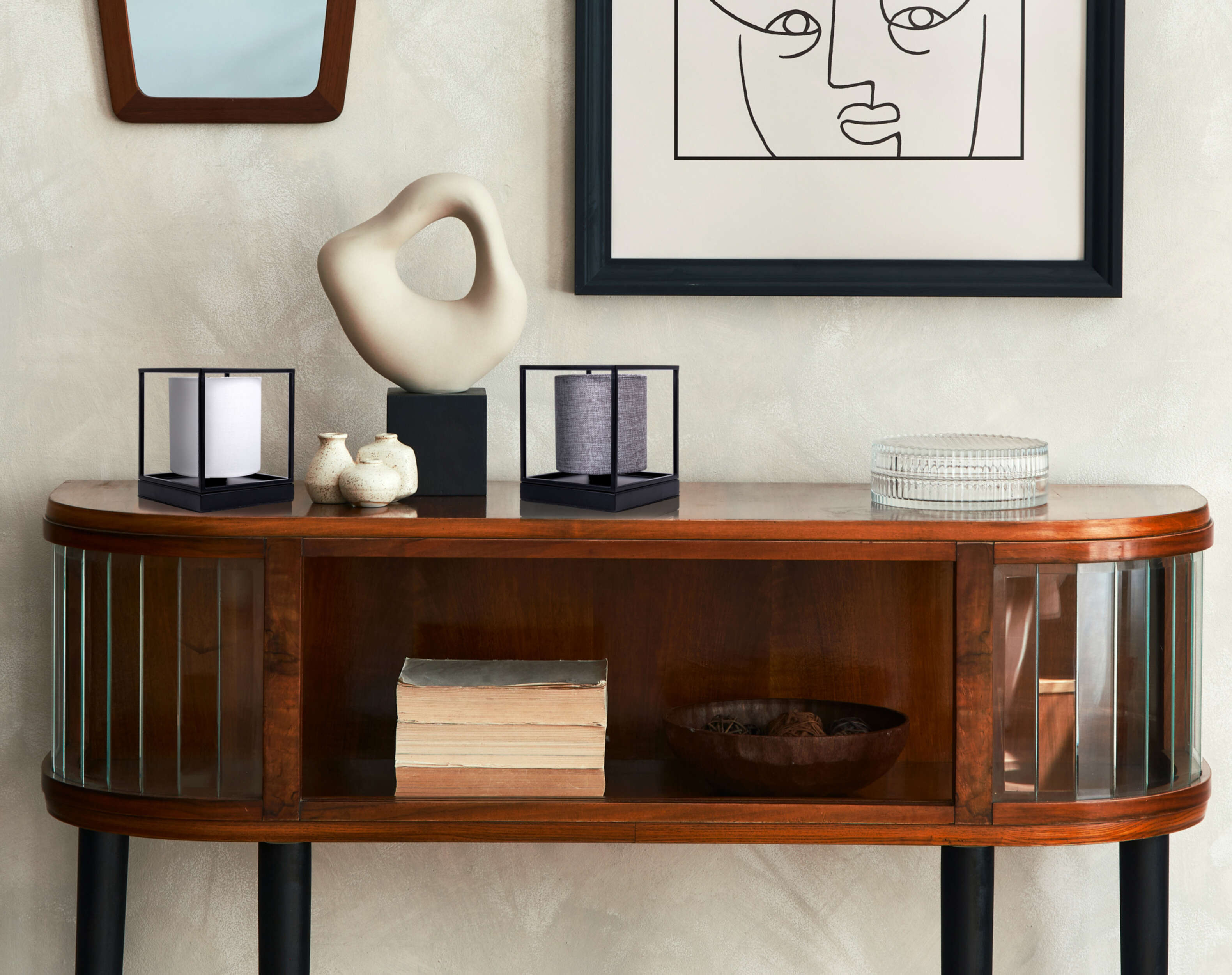 Dekorierter Holzschrank mit Kunst und Objekten. Weißer Wandhintergrund.