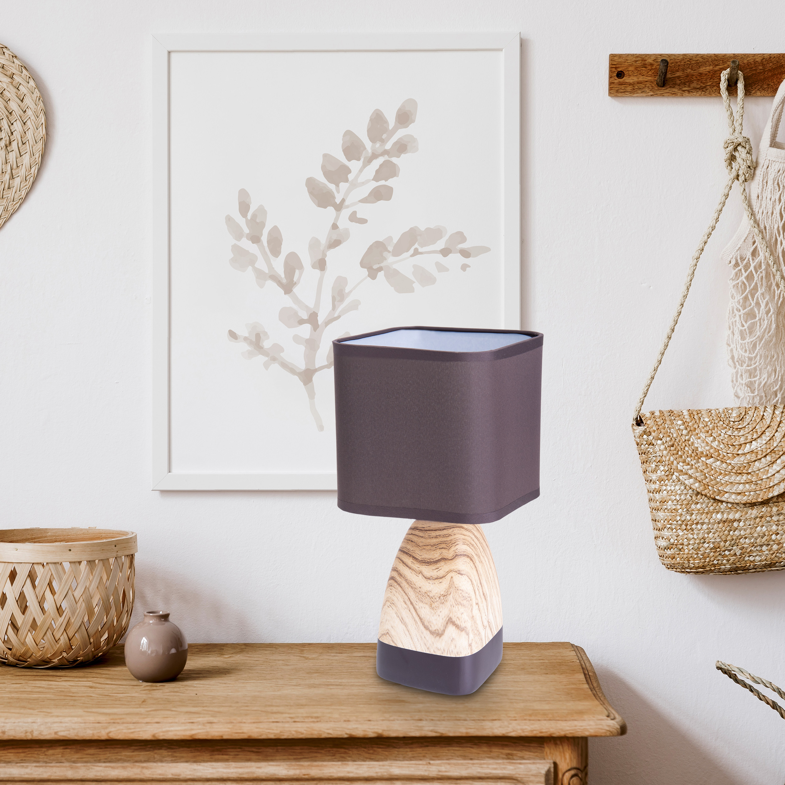 Eine Lampe mit braunem Schirm steht auf einem Holztisch. Dahinter ein Gemälde, daneben ein Korb.